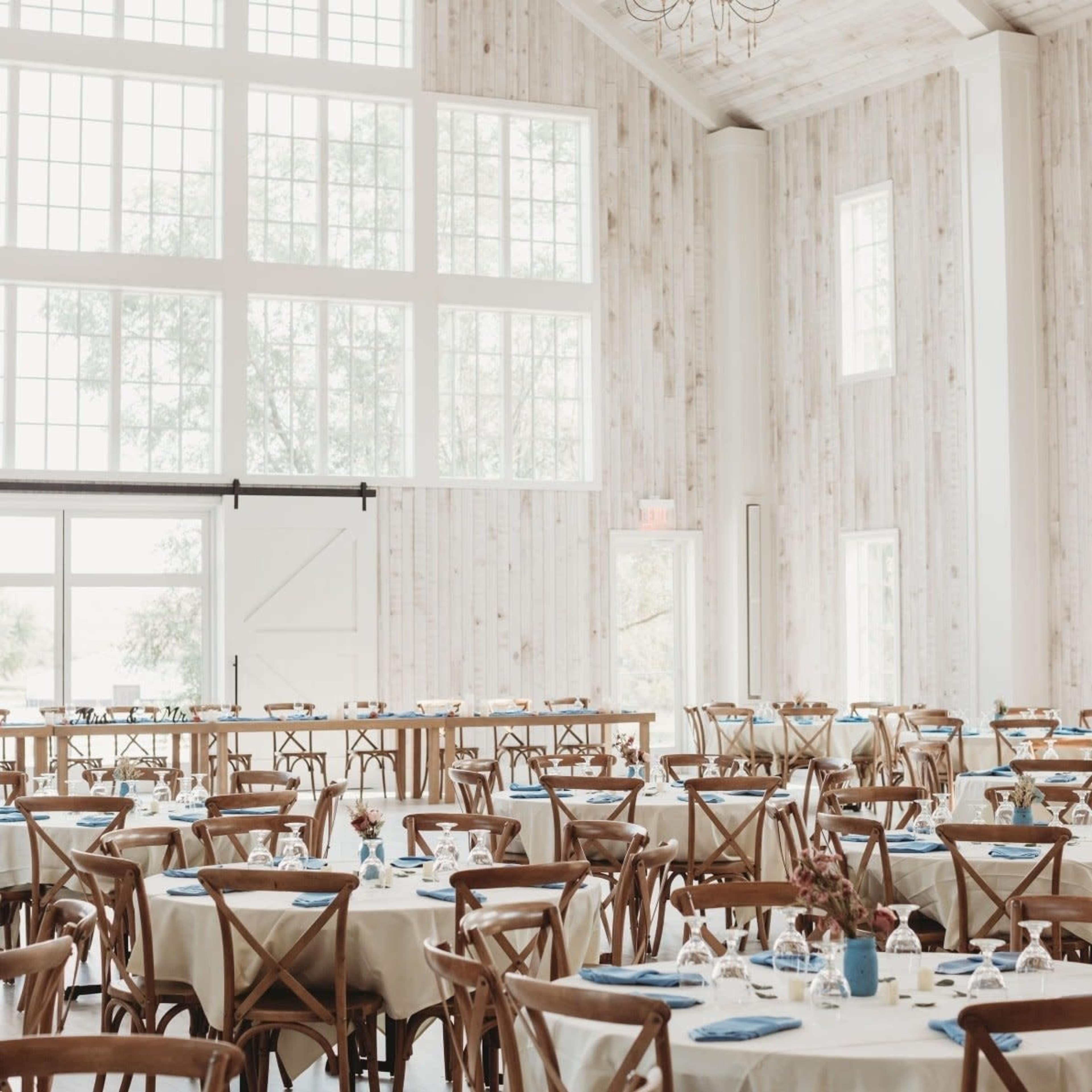 The image shows a spacious dining area with wooden tables and chairs arranged neatly under large windows.