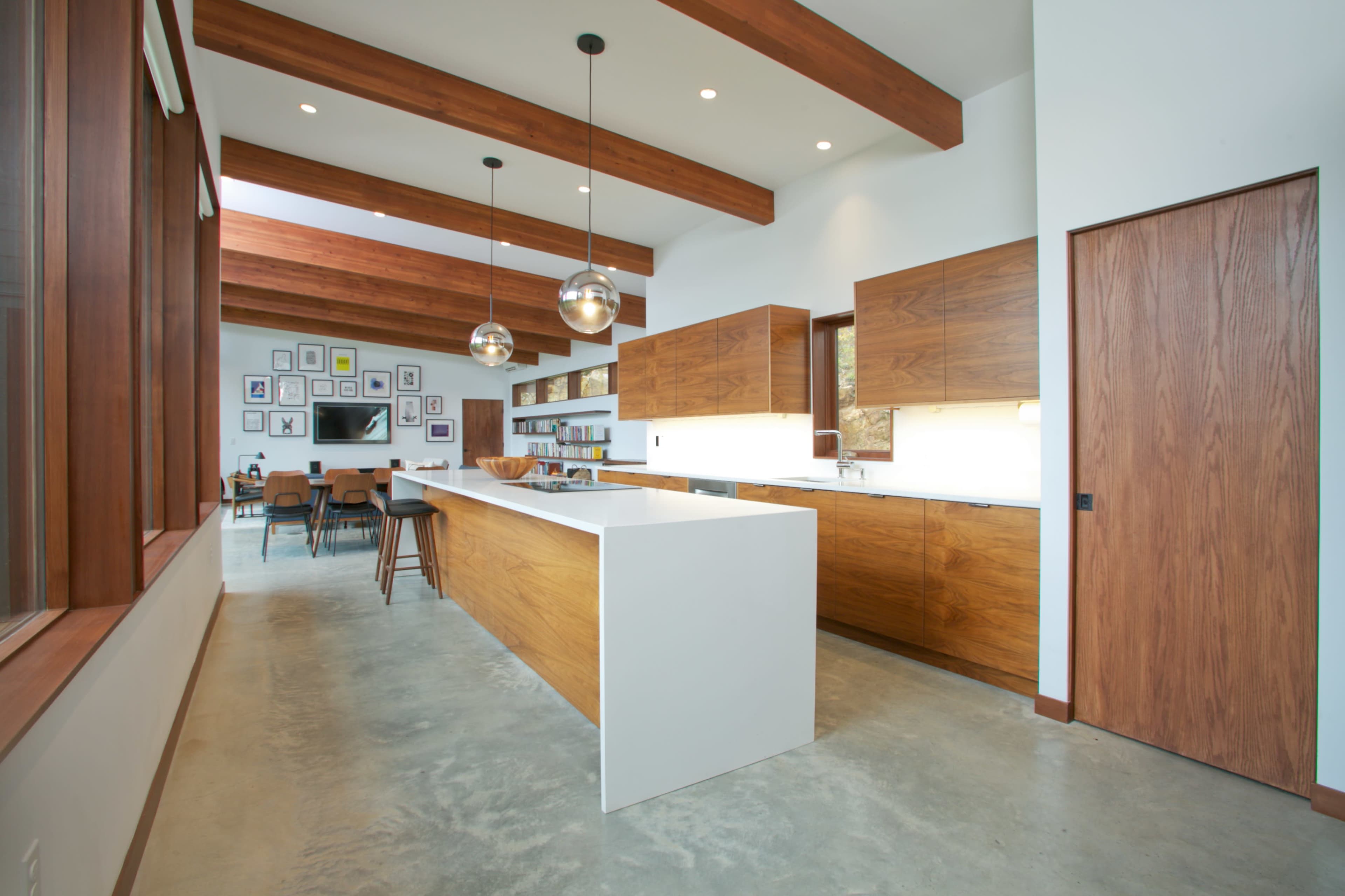 A modern kitchen with wooden cabinets, a large white island, and exposed wooden beams overhead.