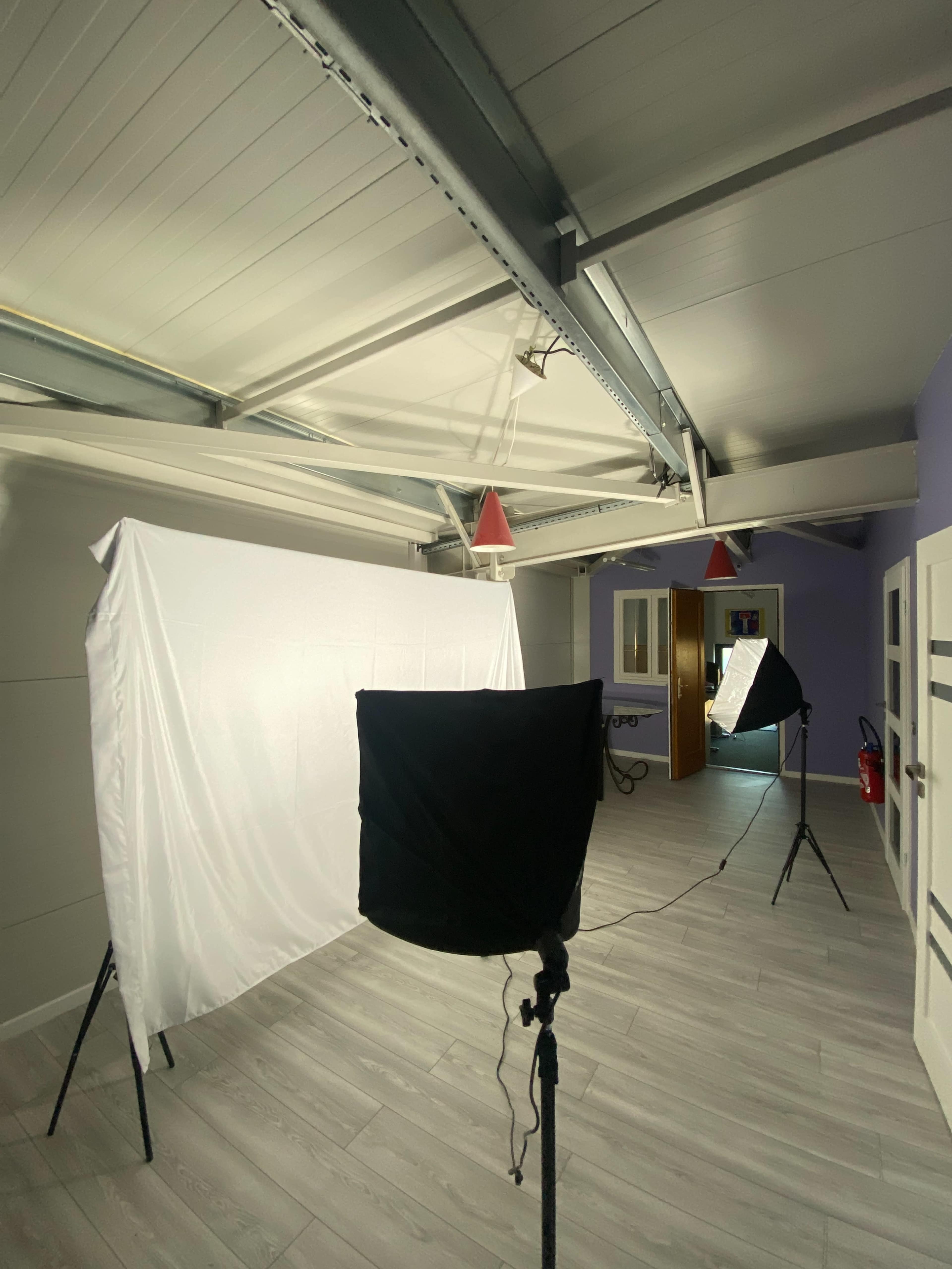 The image shows a spacious room with a white backdrop set up for photography, along with two softbox lights positioned in front of it.