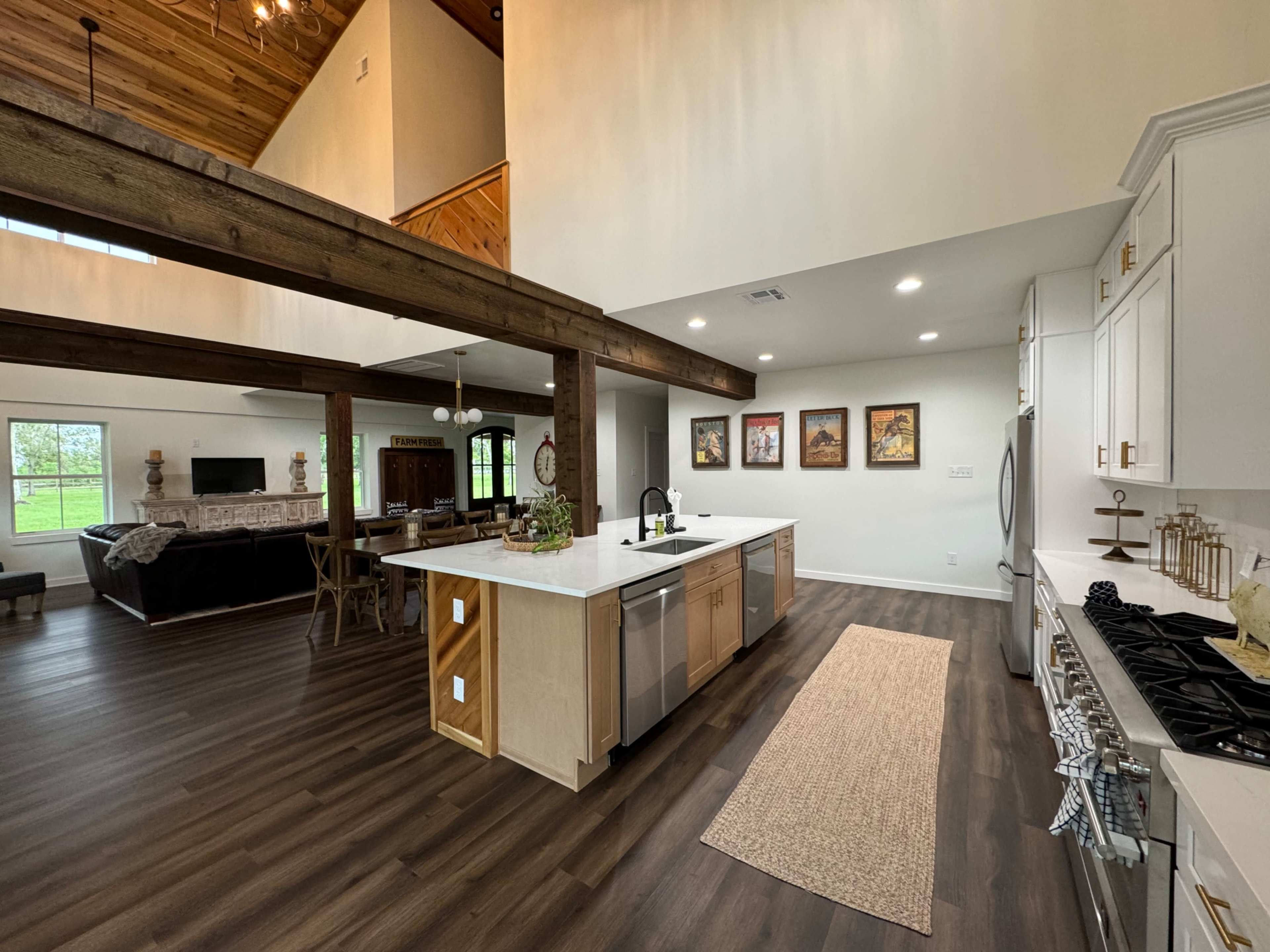 A modern kitchen with an island, stainless steel appliances, and a view of a living area featuring wooden beams and large windows.