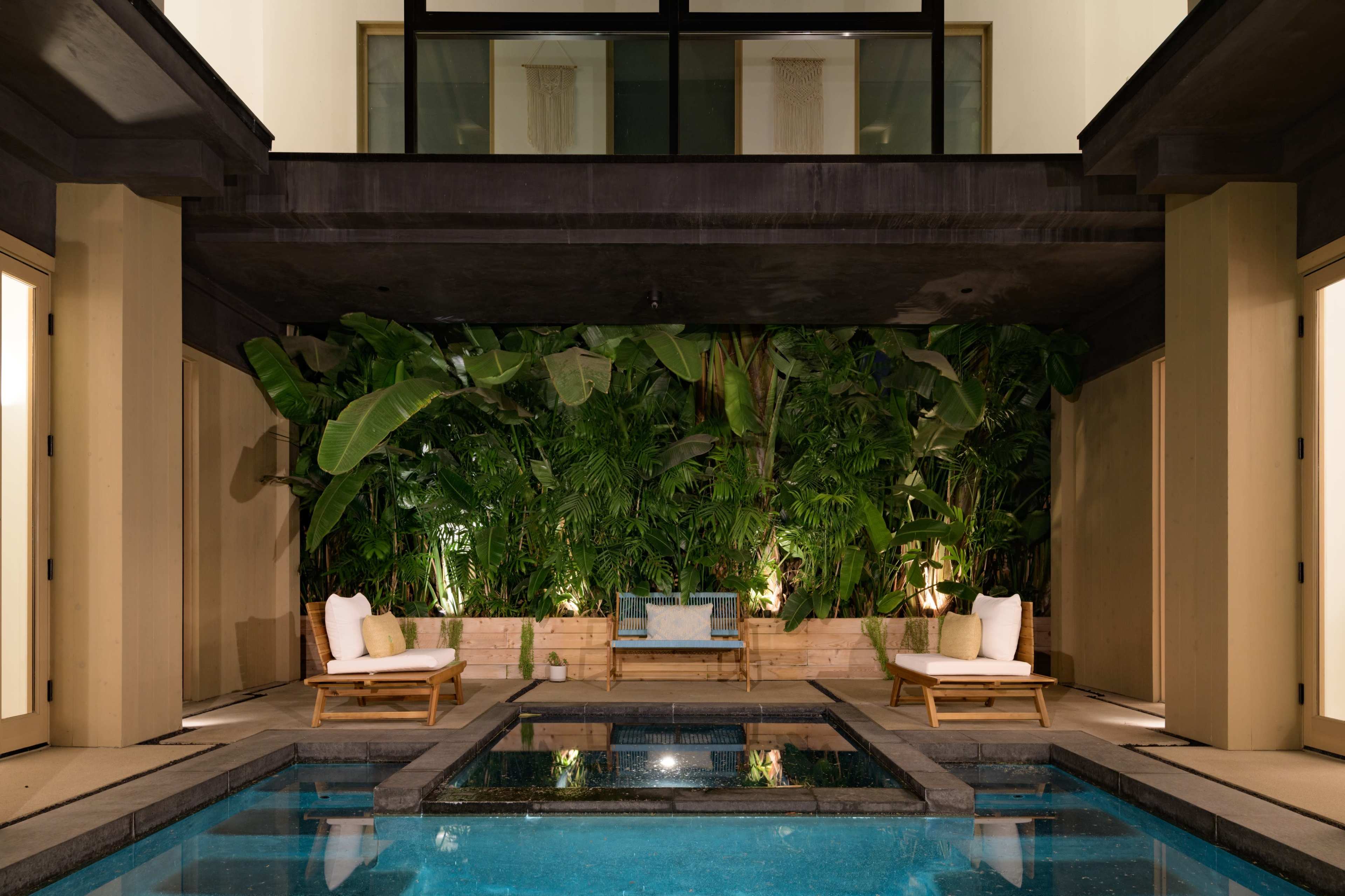 A modern courtyard with a swimming pool surrounded by lush greenery and two seating areas.