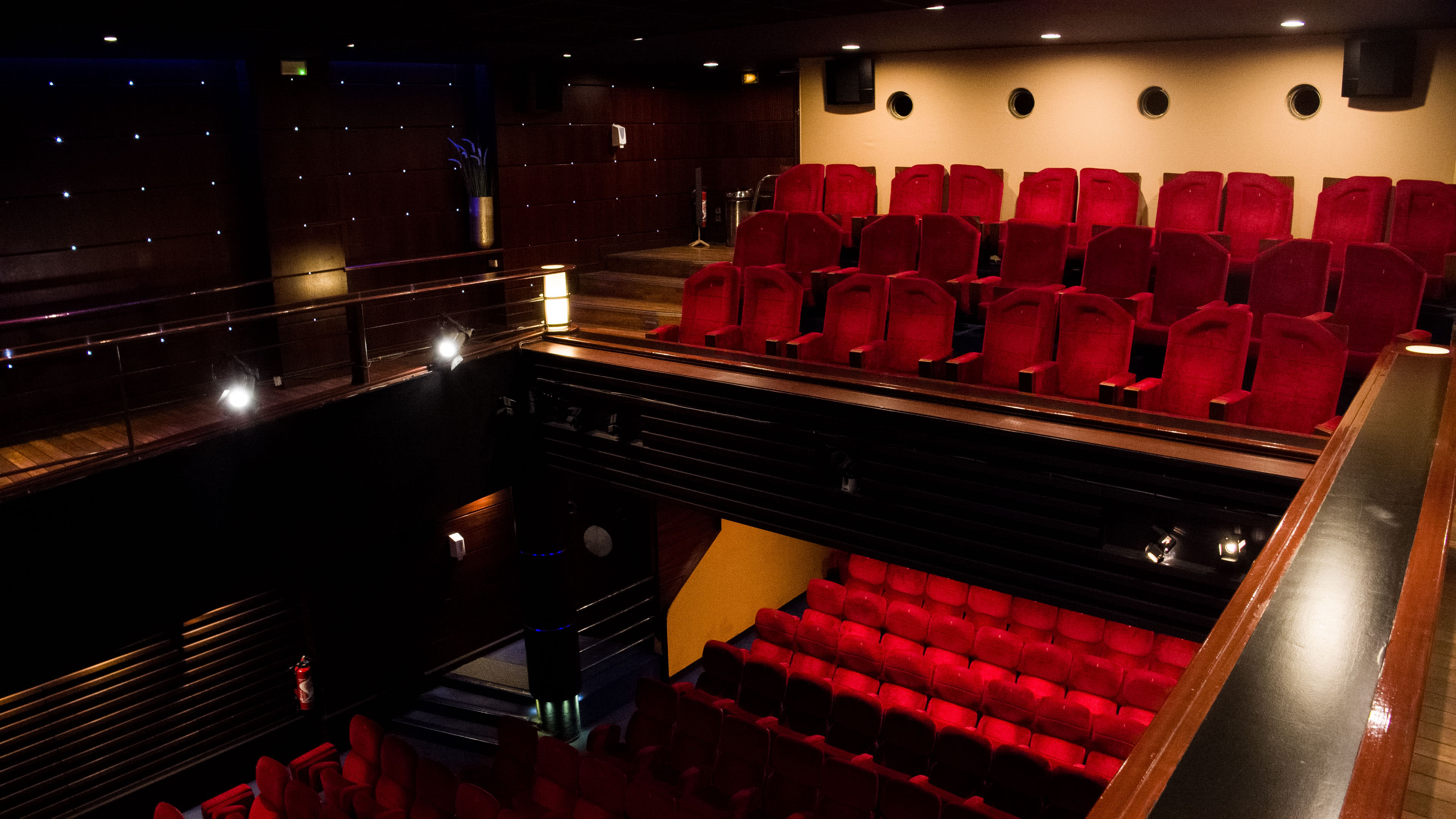 A multi-level theater with red seating and dim lighting.