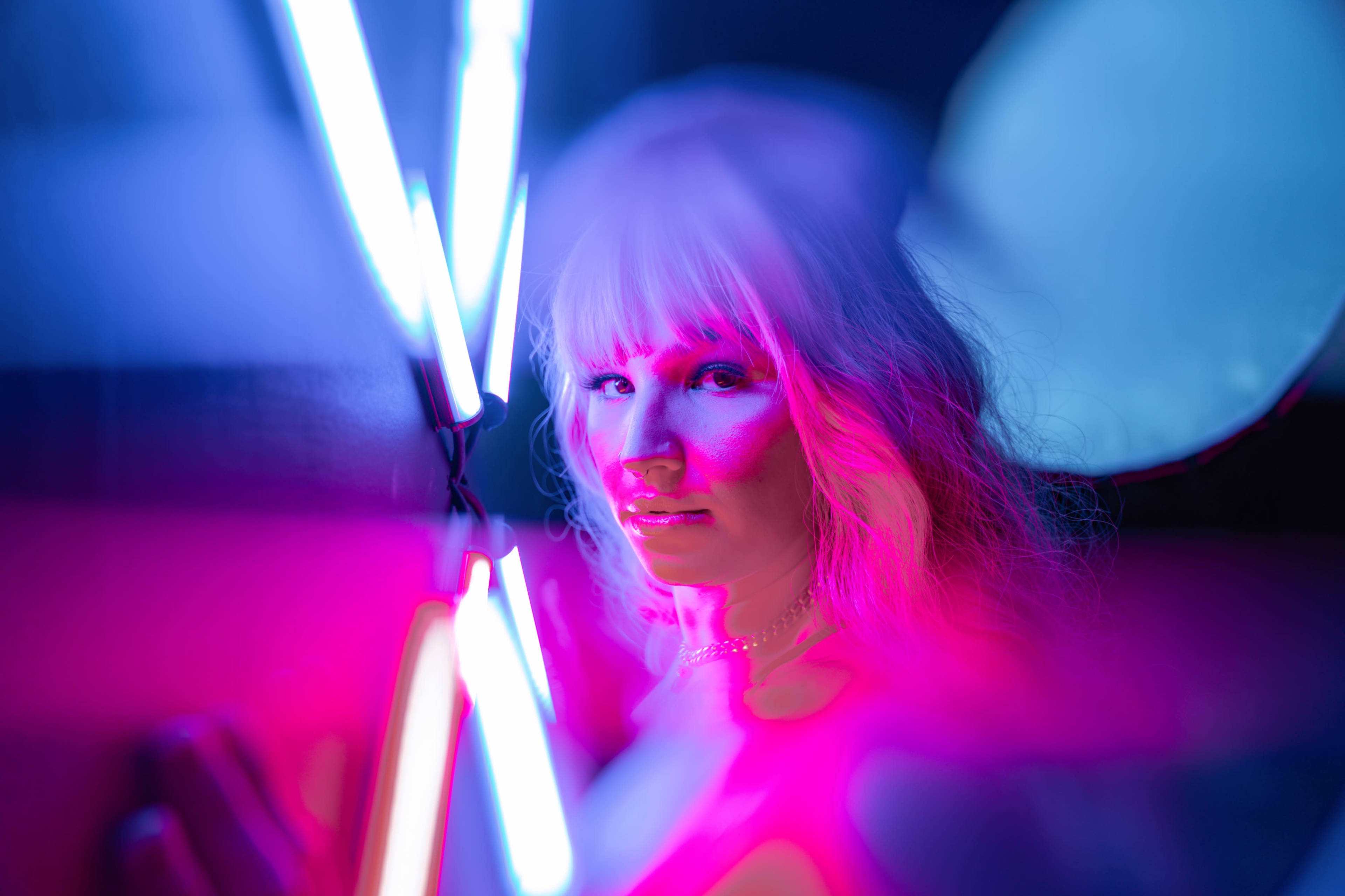 A person with long light hair is illuminated by colorful neon lights in a dim environment.