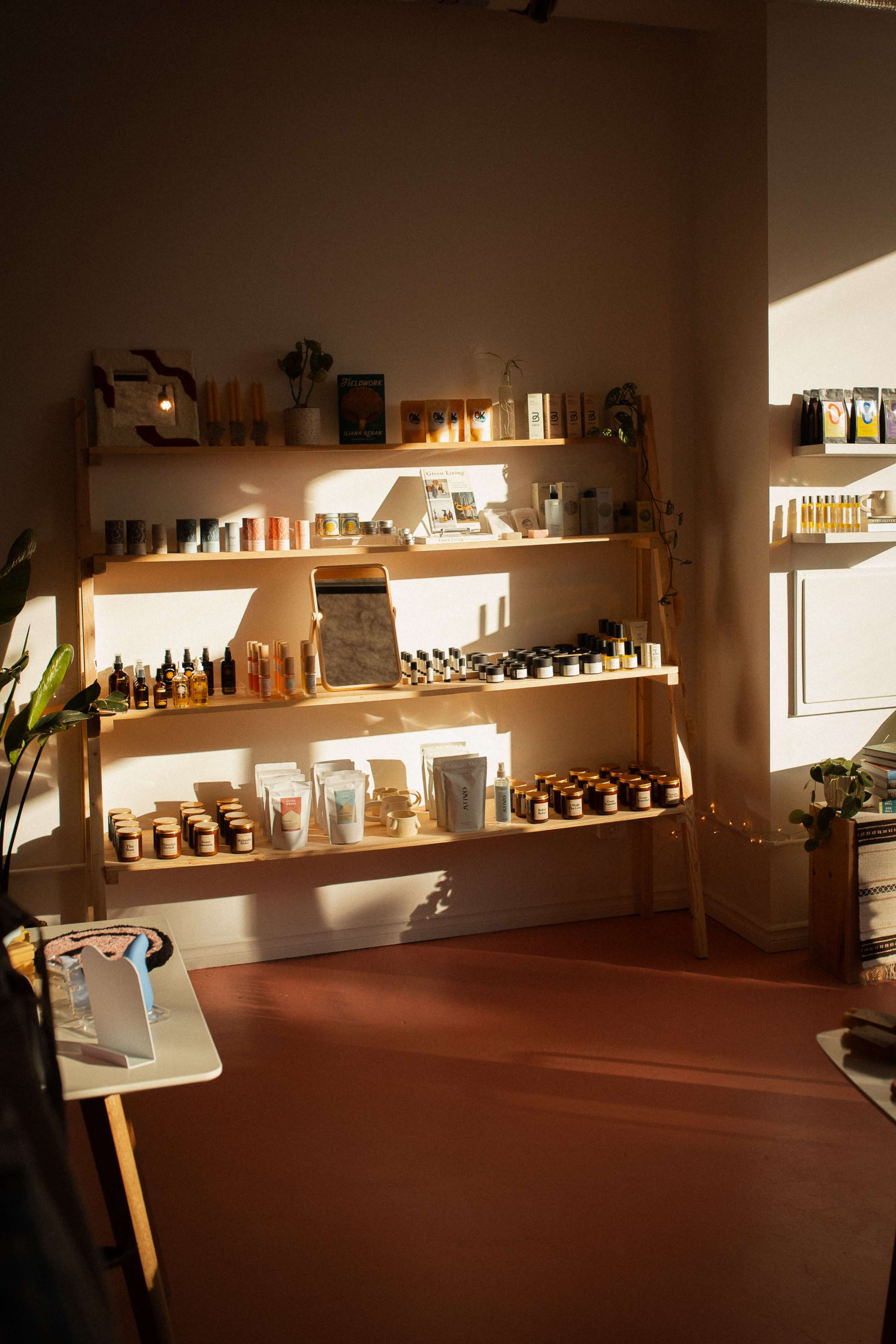 A wooden shelf displays a variety of beauty products, including oils, creams, and jars, illuminated by natural light streaming through a window.