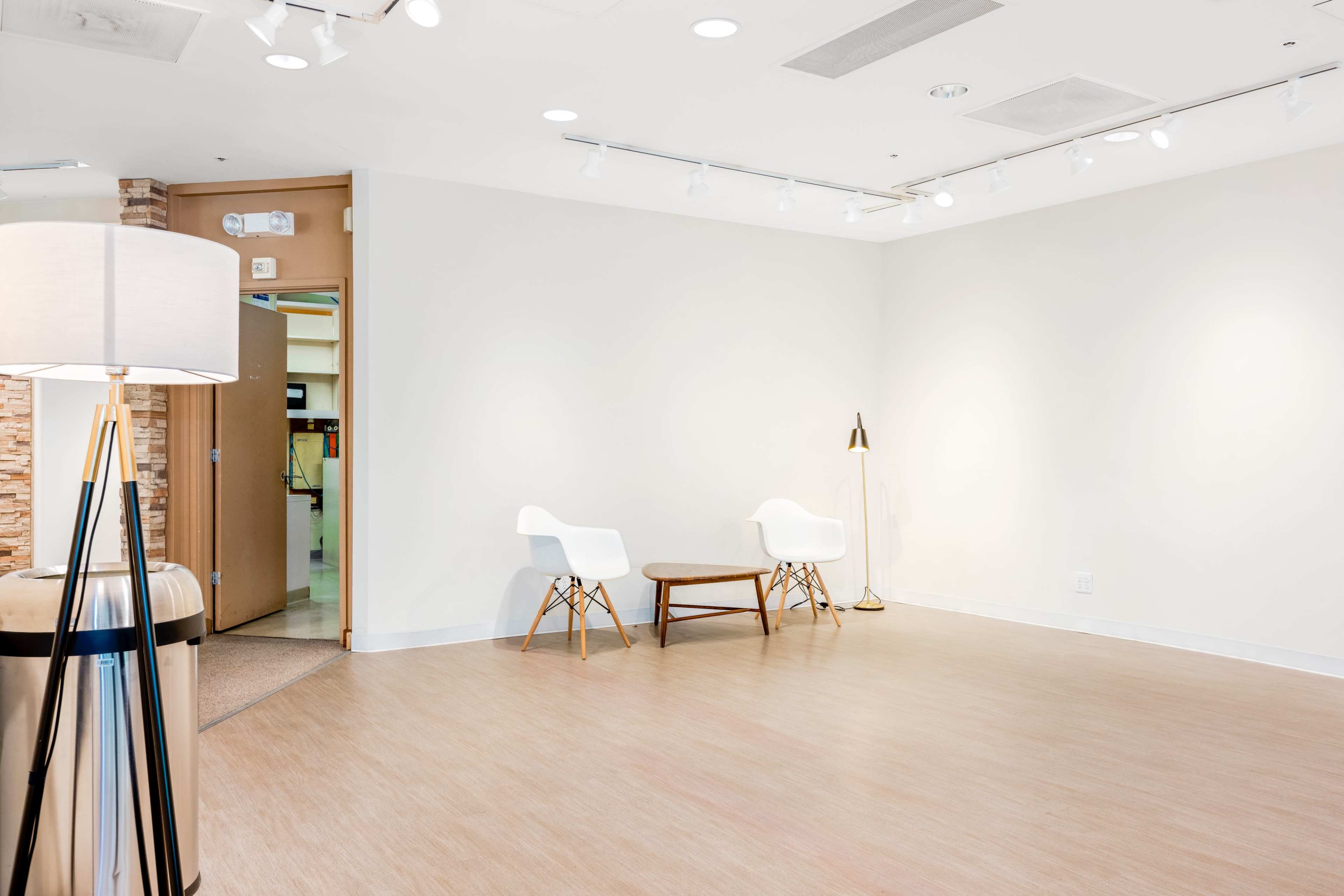 A modern, empty room with two white chairs, a wooden coffee table, and a lamp, featuring bright lighting and a light-colored floor.