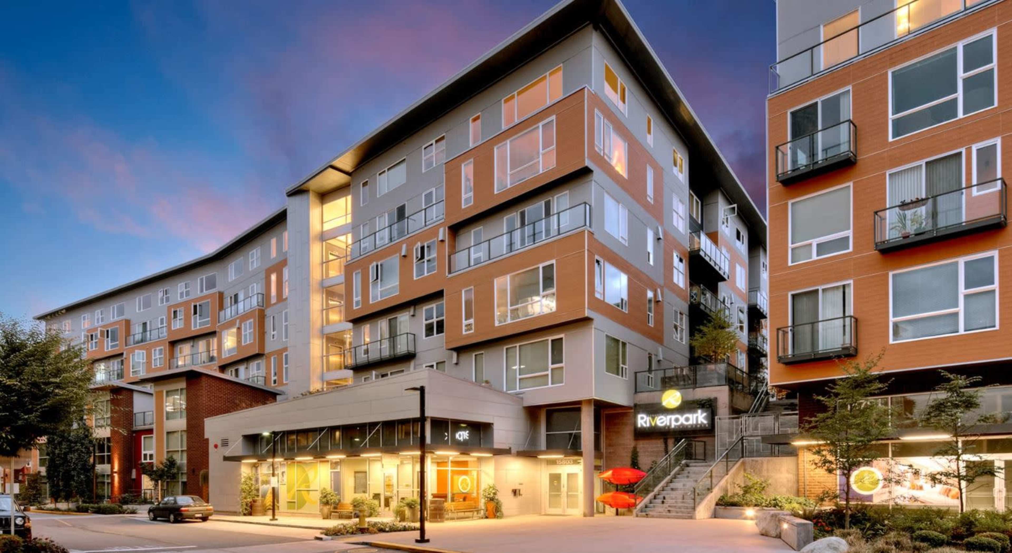 A multi-story residential building with a modern facade features large windows and a prominent entrance with the name "Riverpark" displayed.