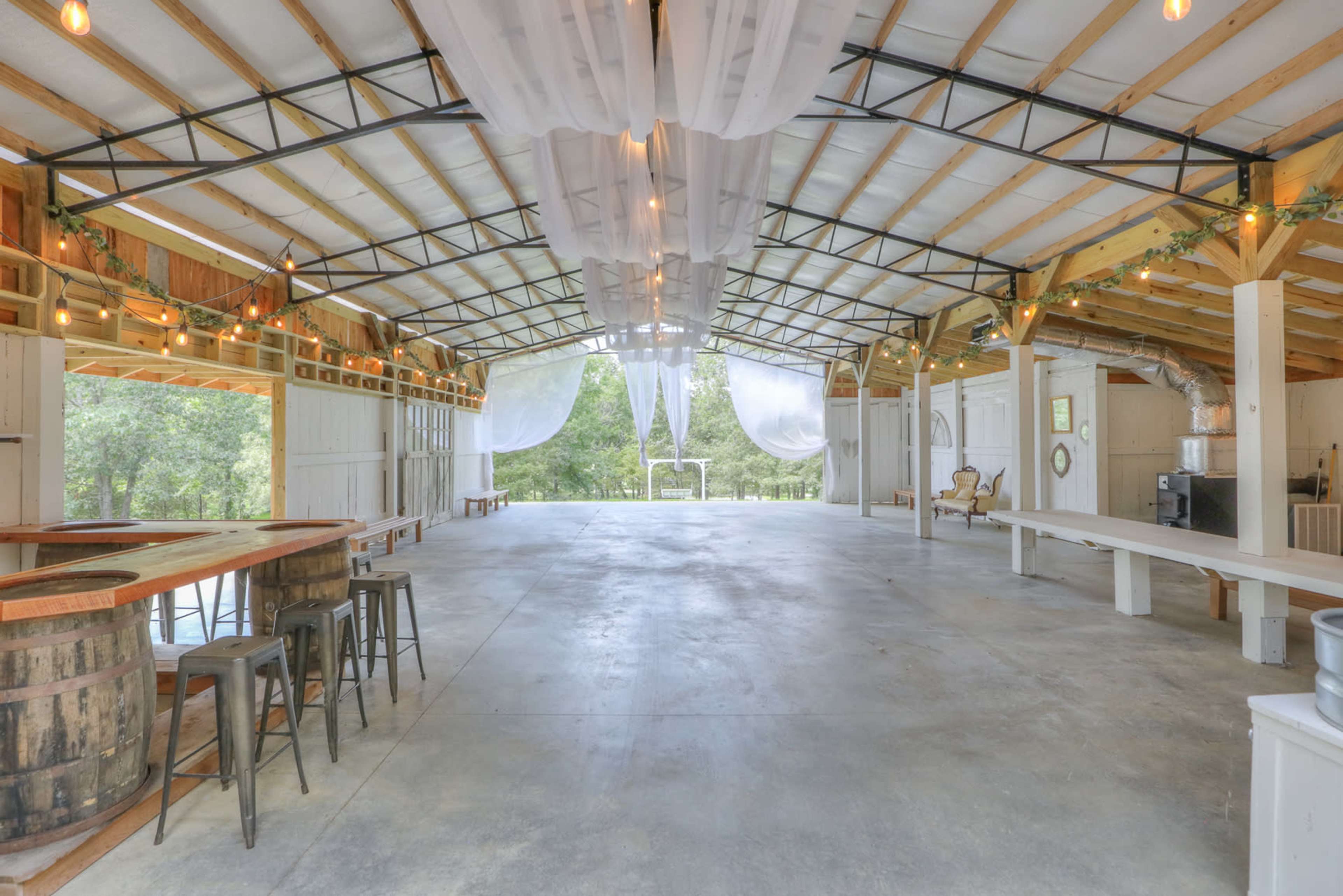 A spacious indoor venue with a high ceiling, exposed wooden beams, and decorative drapery, featuring a wooden bar and seating areas.