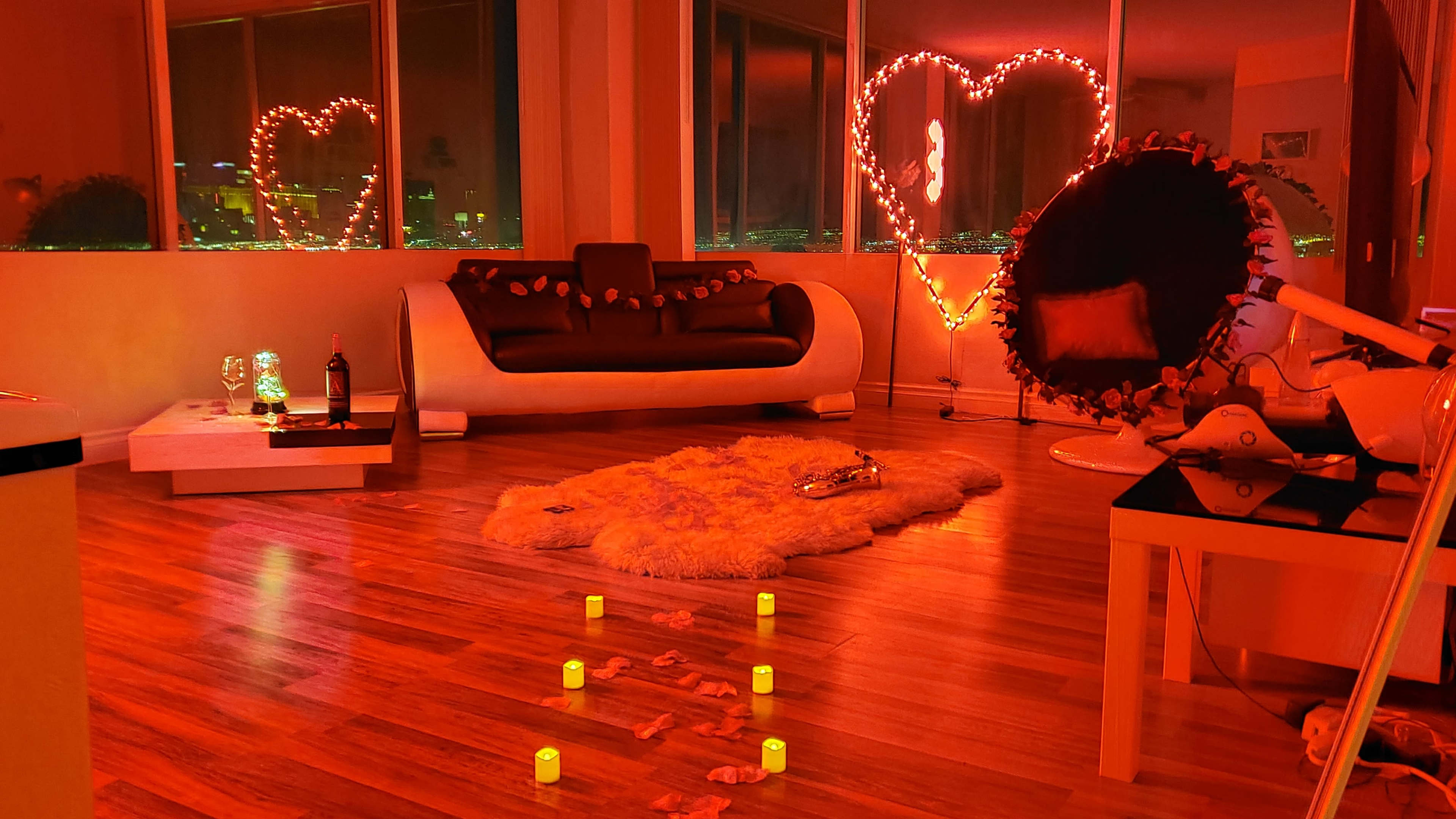 The image shows a modern living room with a heart-shaped light display, a black sofa, and a white coffee table, all illuminated by warm red lighting.