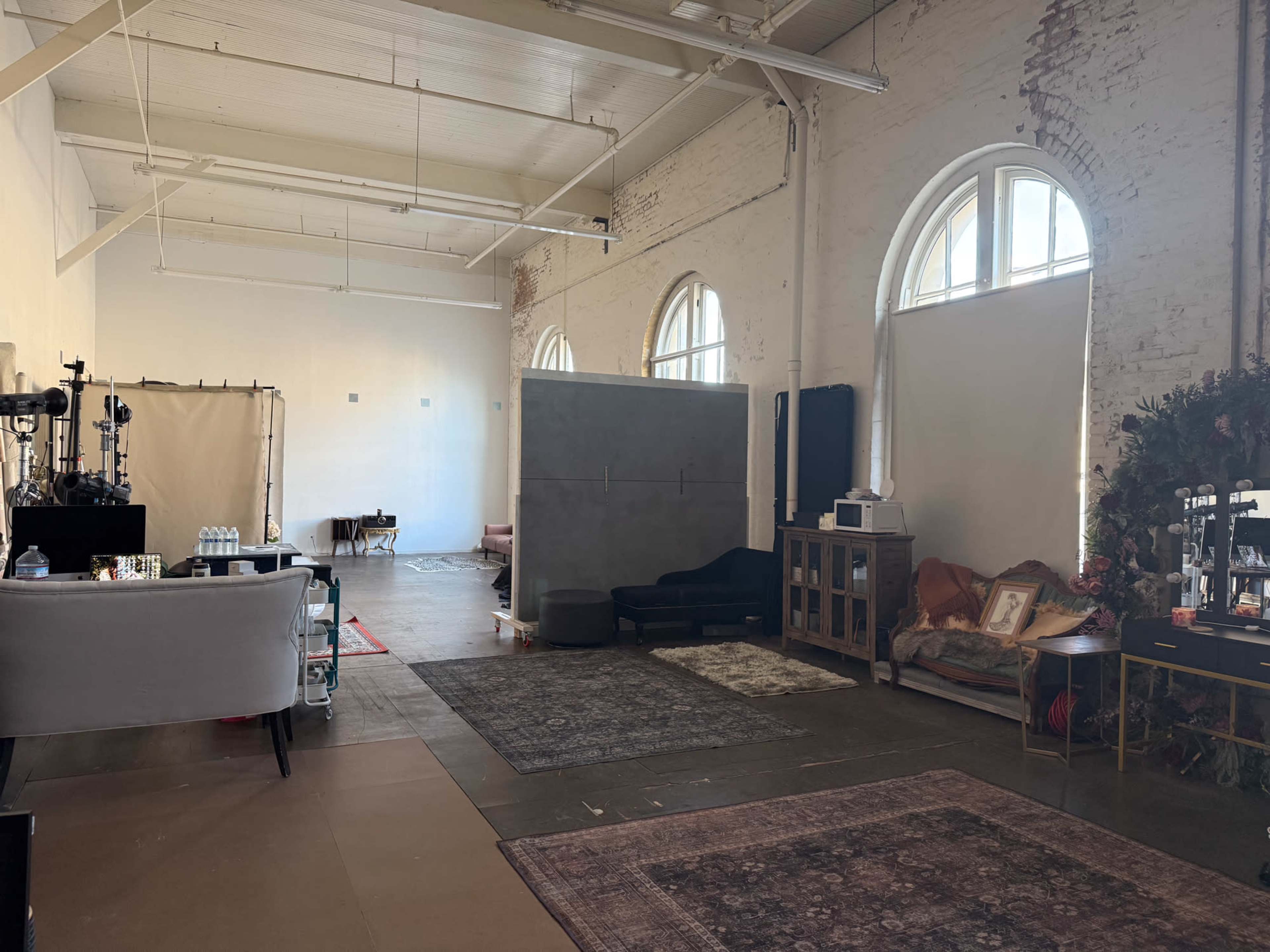 The image shows an industrial space with large windows, featuring a mix of furniture, decorative elements, and a partition wall.