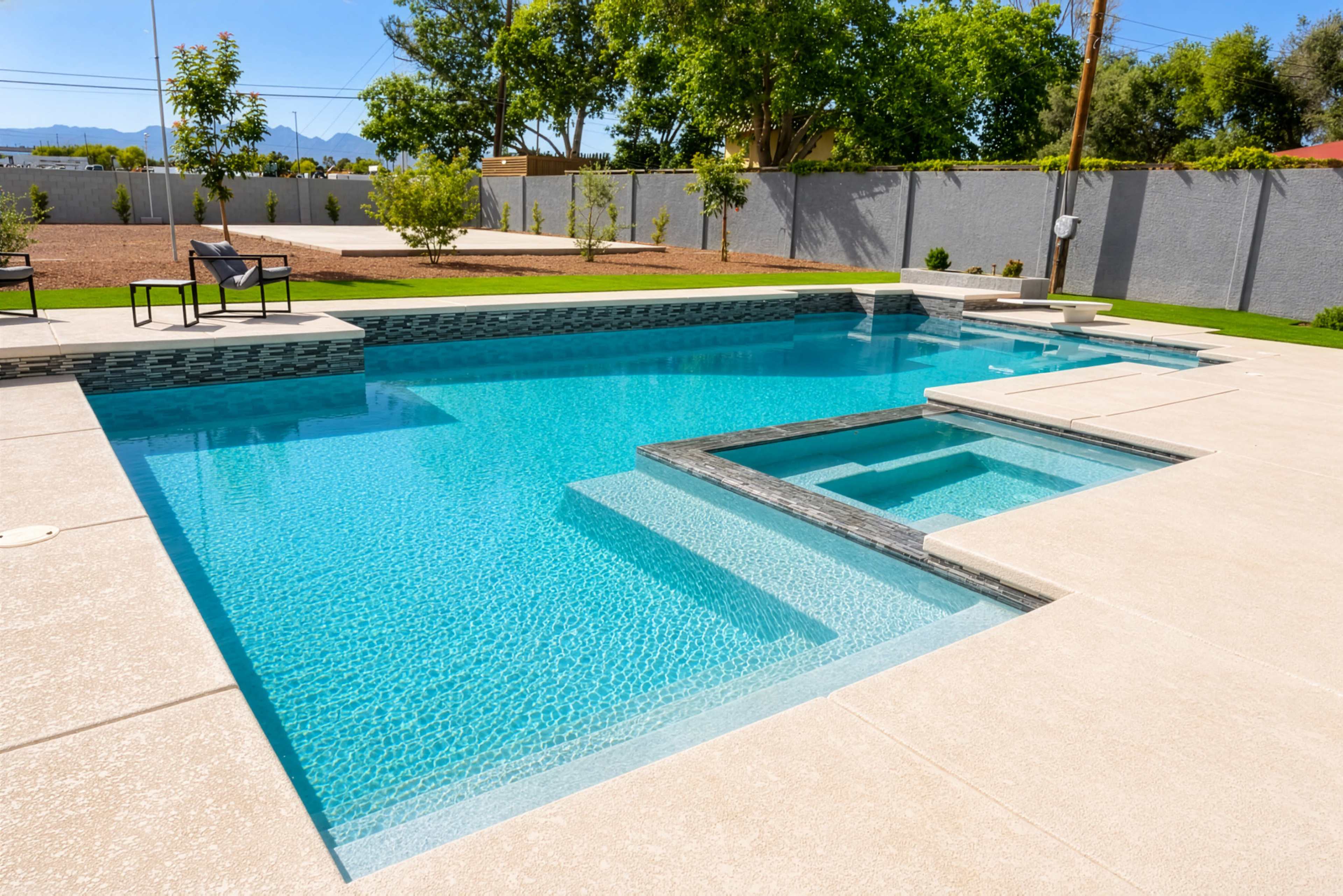 The image shows a modern swimming pool with a spa feature, surrounded by a patio and landscaped greenery.