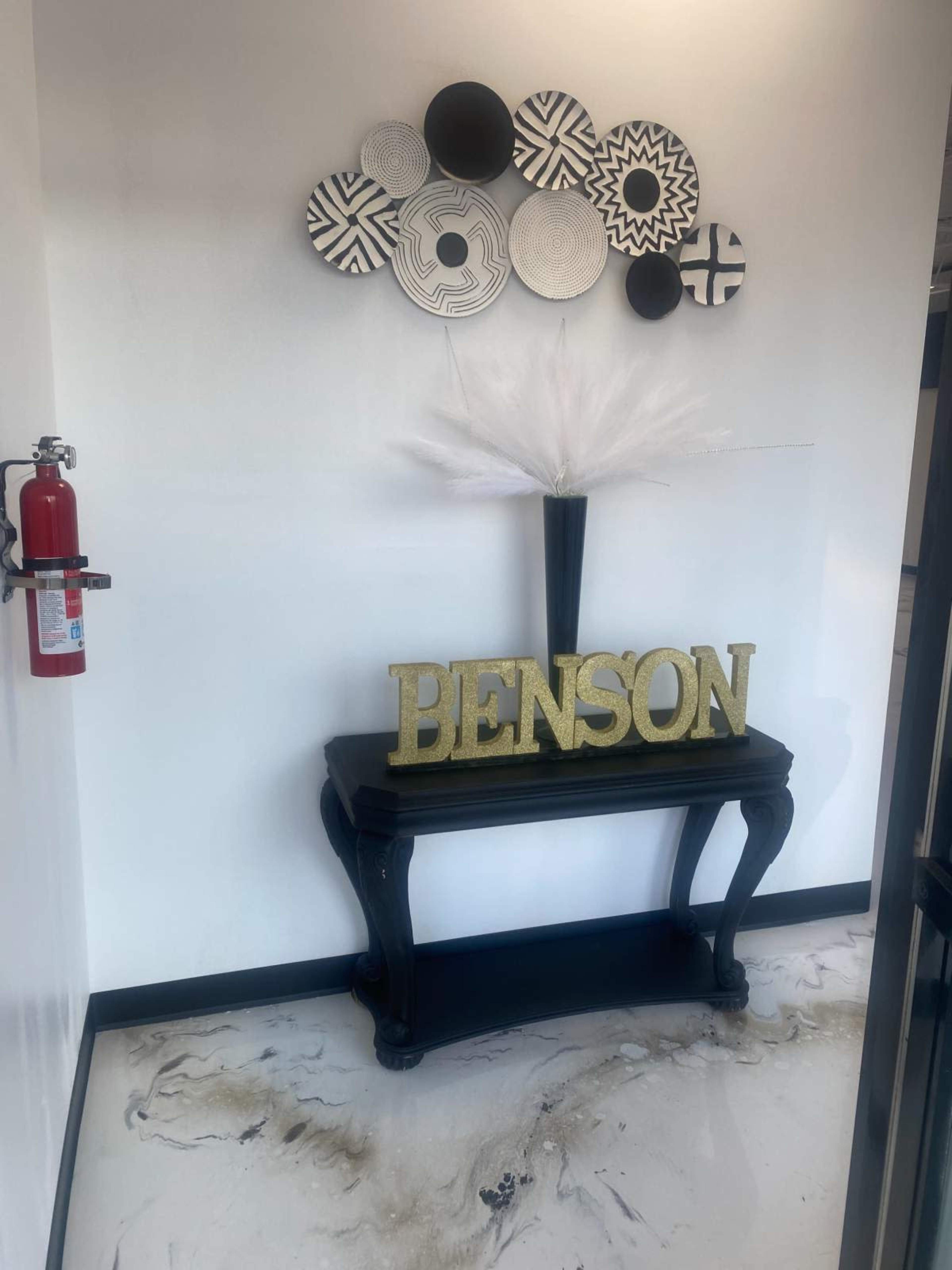 A black console table displaying the name "BENSON" in large golden letters, positioned under a wall adorned with various circular decorative pieces.