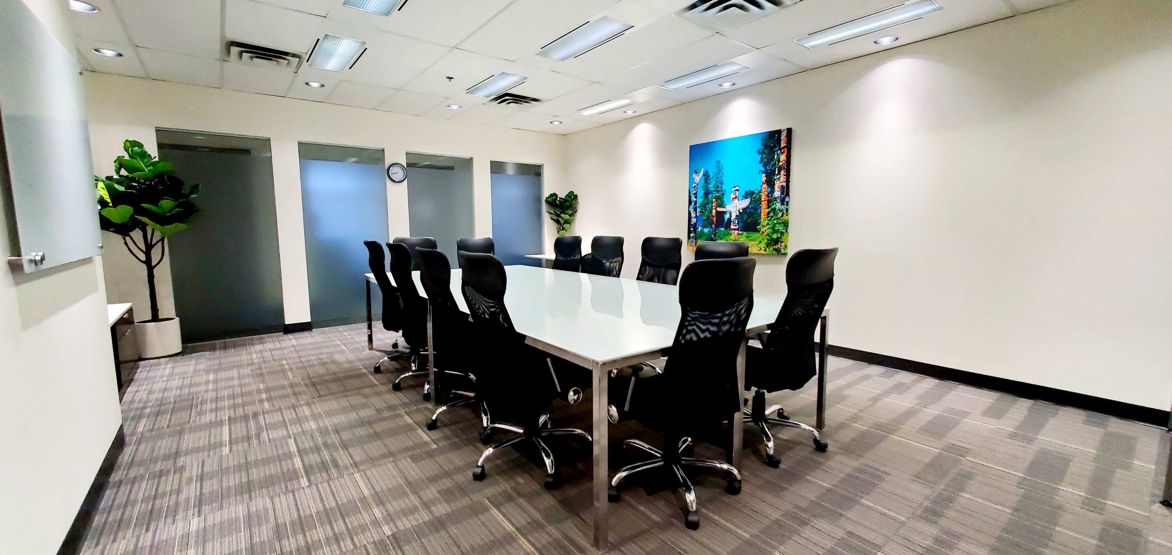 A modern conference room features a long table surrounded by ergonomic chairs, with a large wall art piece and plants decorating the space.