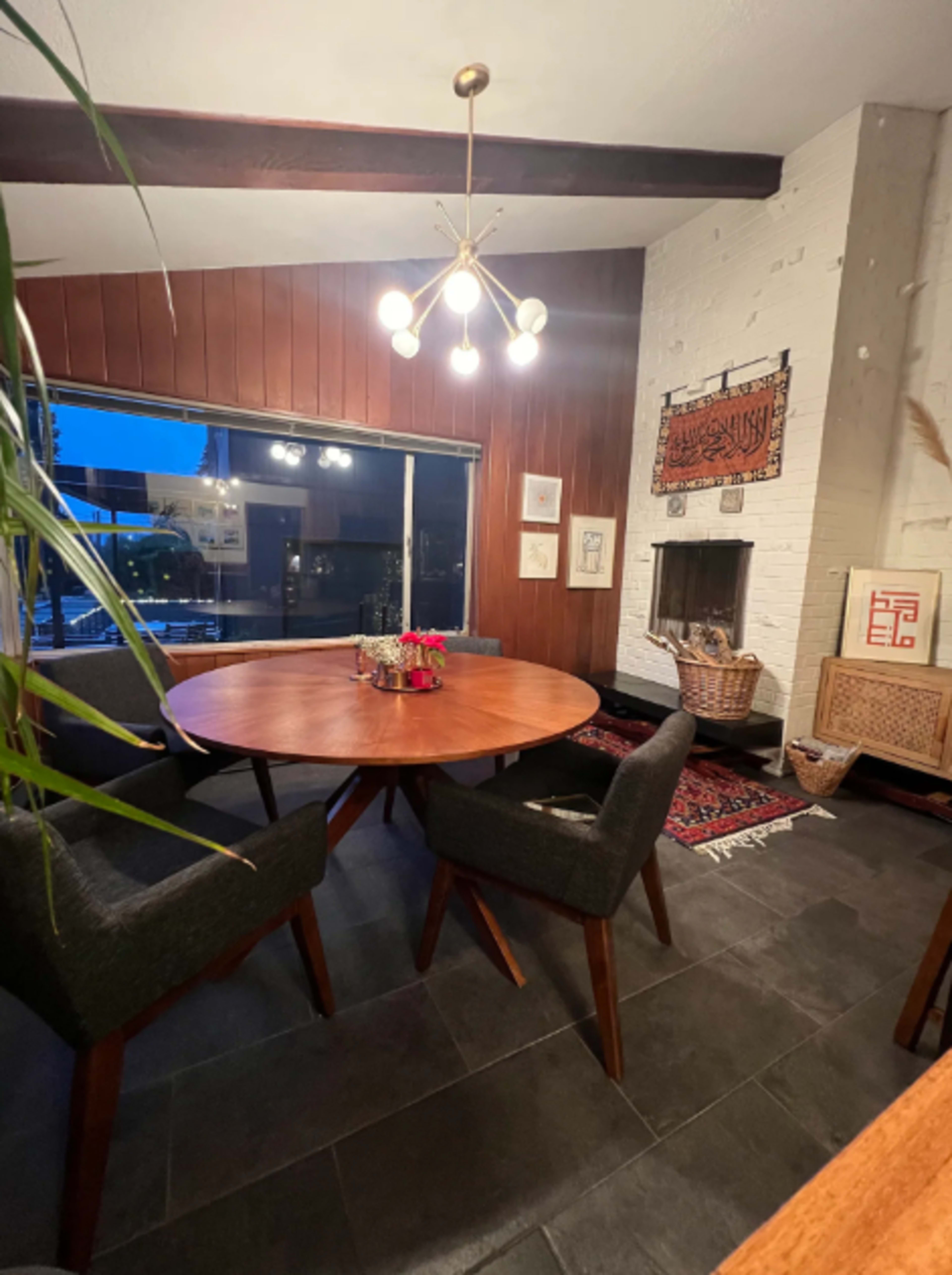 A wooden dining table with four chairs is set near a fireplace, with a woven basket and decorative items on display in a cozy interior space.