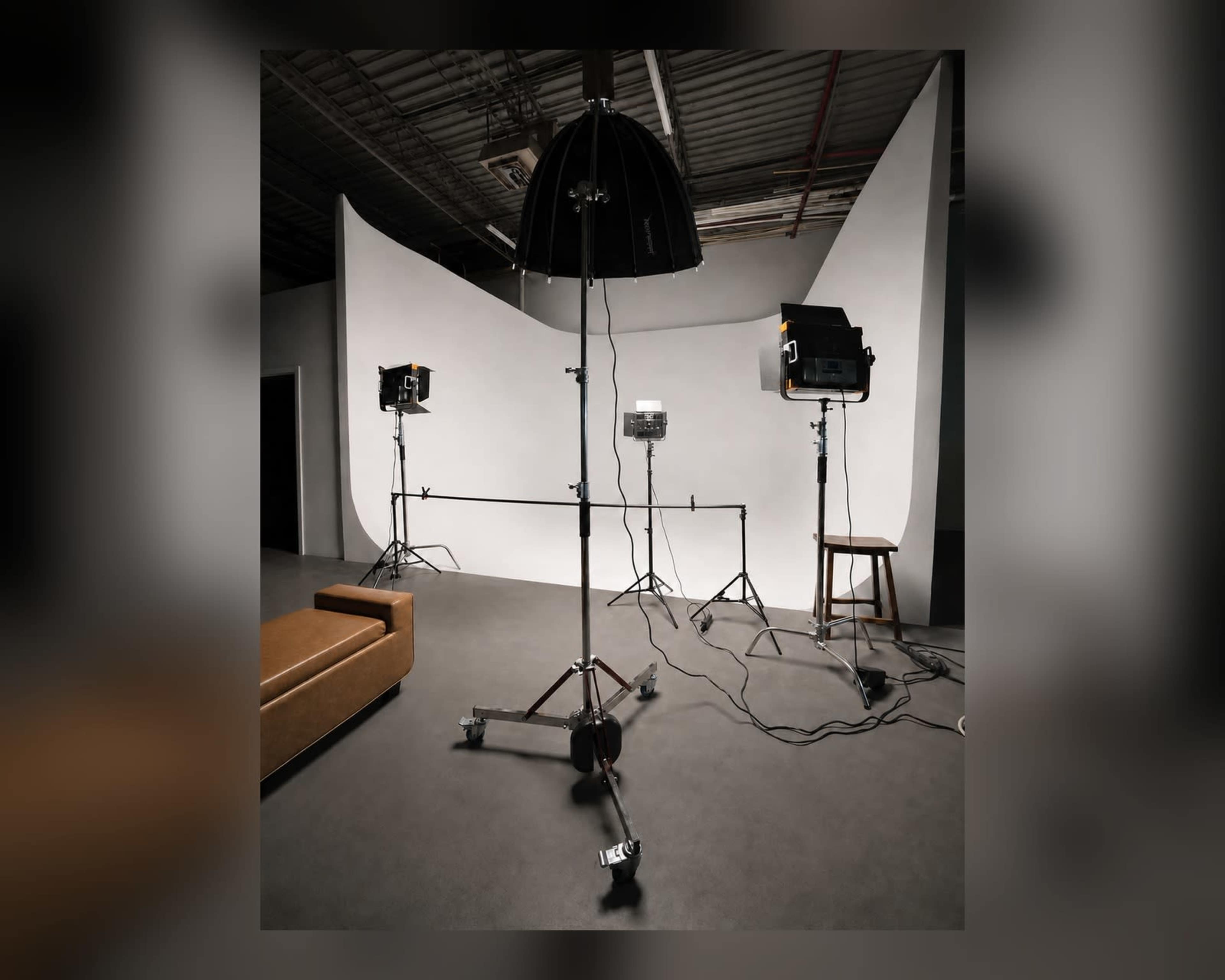 The image shows a photography studio setup featuring lighting equipment and a neutral backdrop.