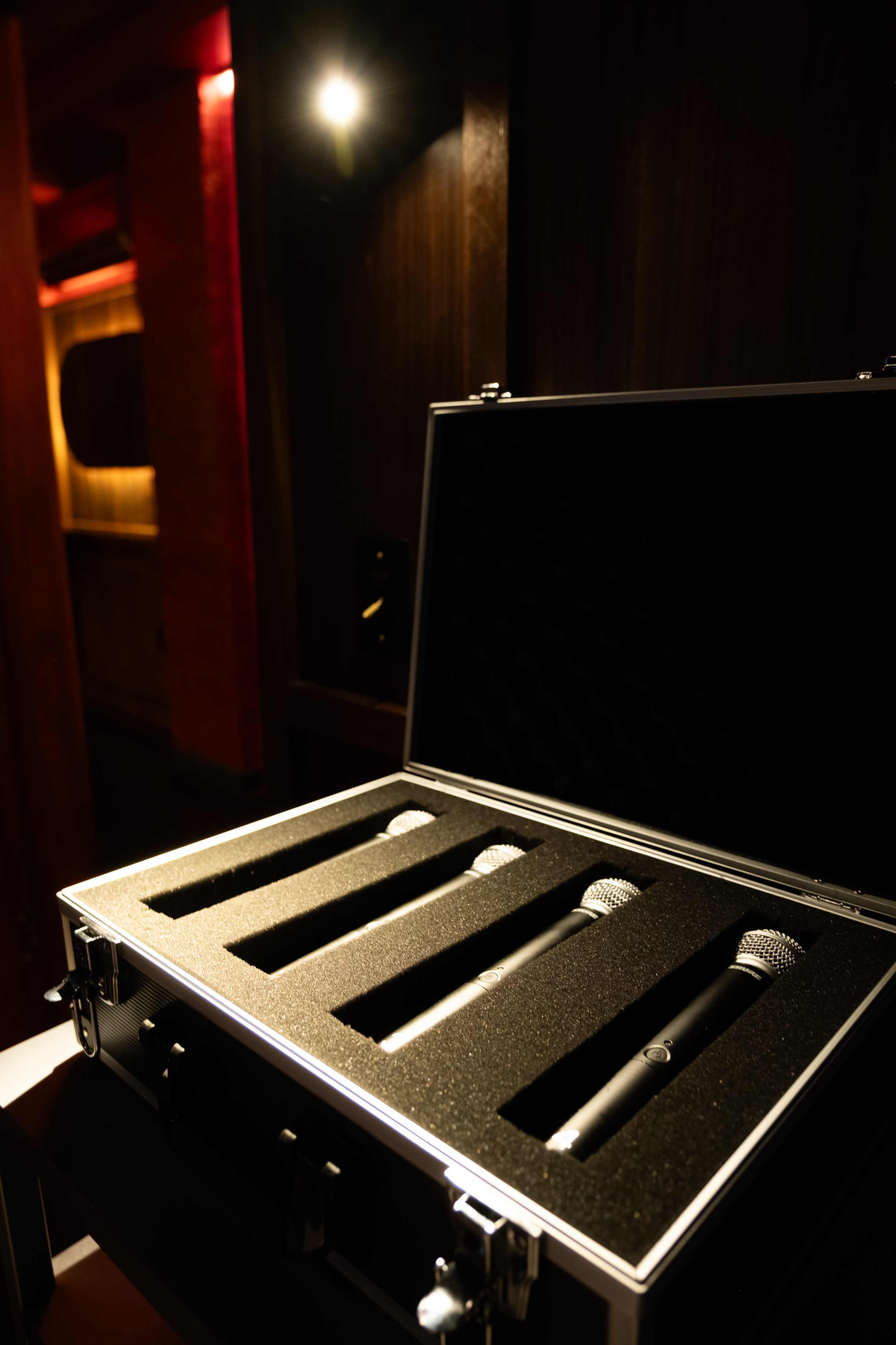 A silver case with black foam interior contains four microphones, positioned neatly in a dimly lit room.