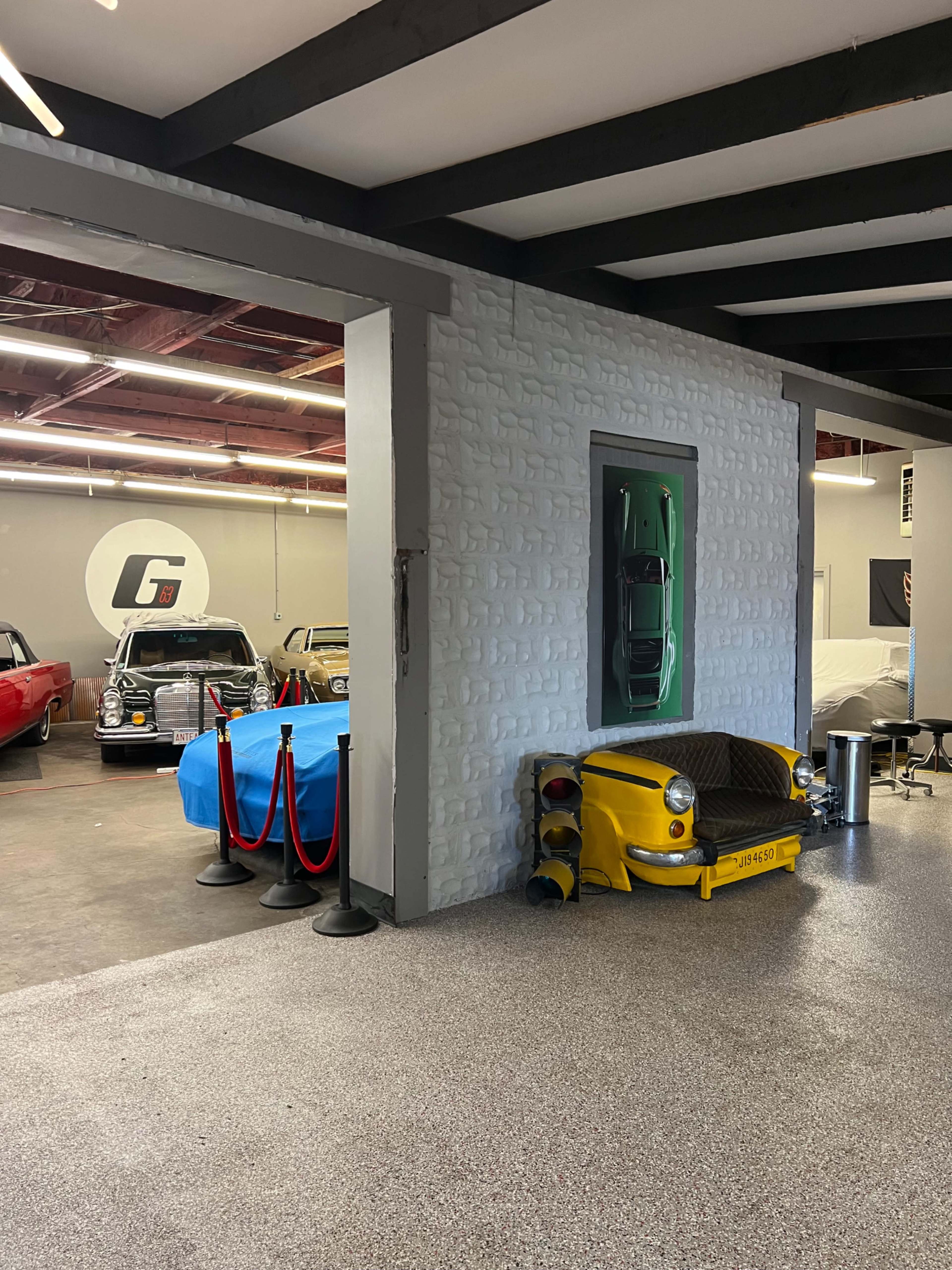 A garage space with multiple classic cars, including a yellow vintage taxi, along with a sectioned-off area featuring blue tarps covering other vehicles.
