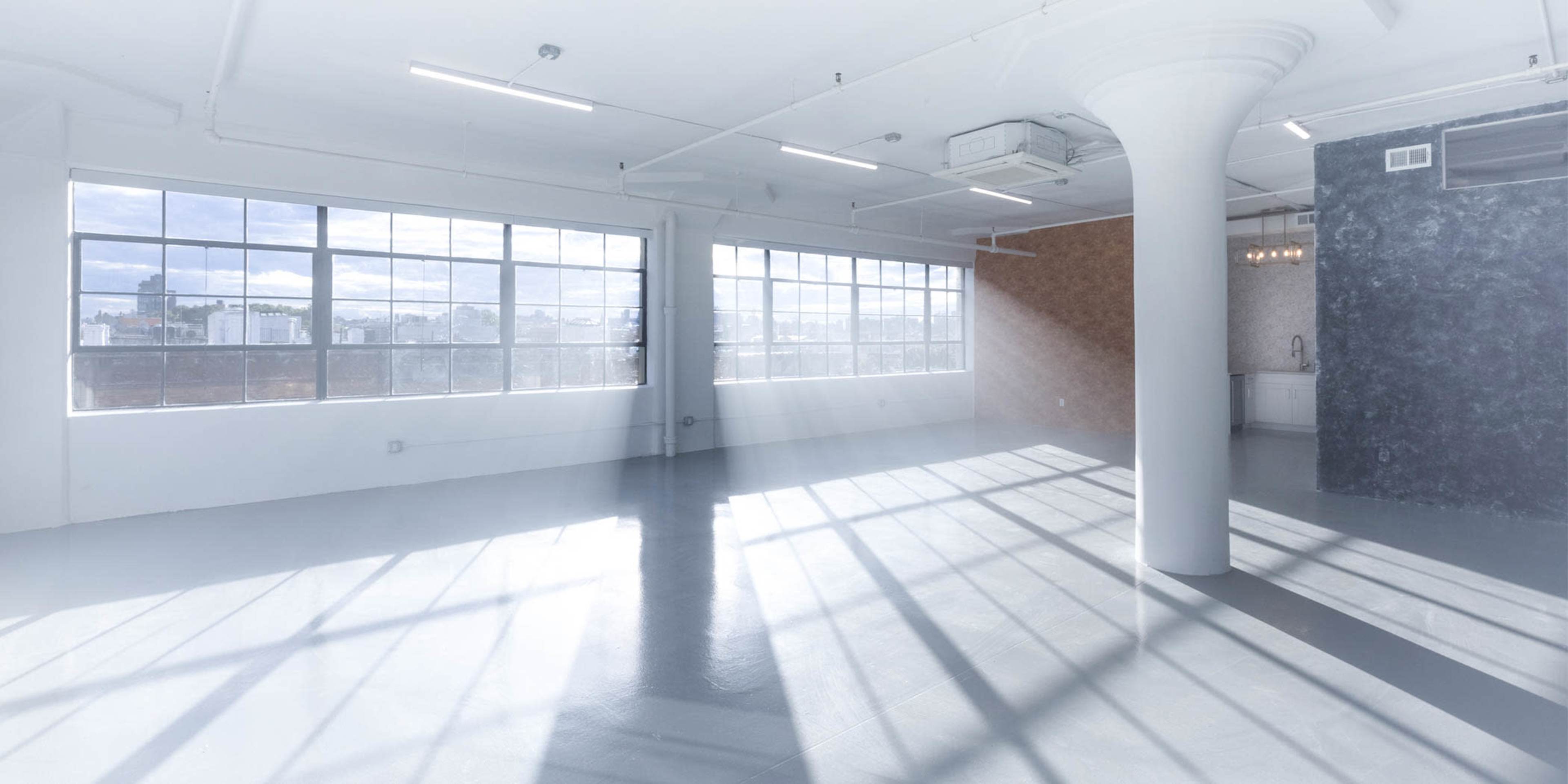 A spacious, well-lit room with large windows casting shadows on the polished floor.