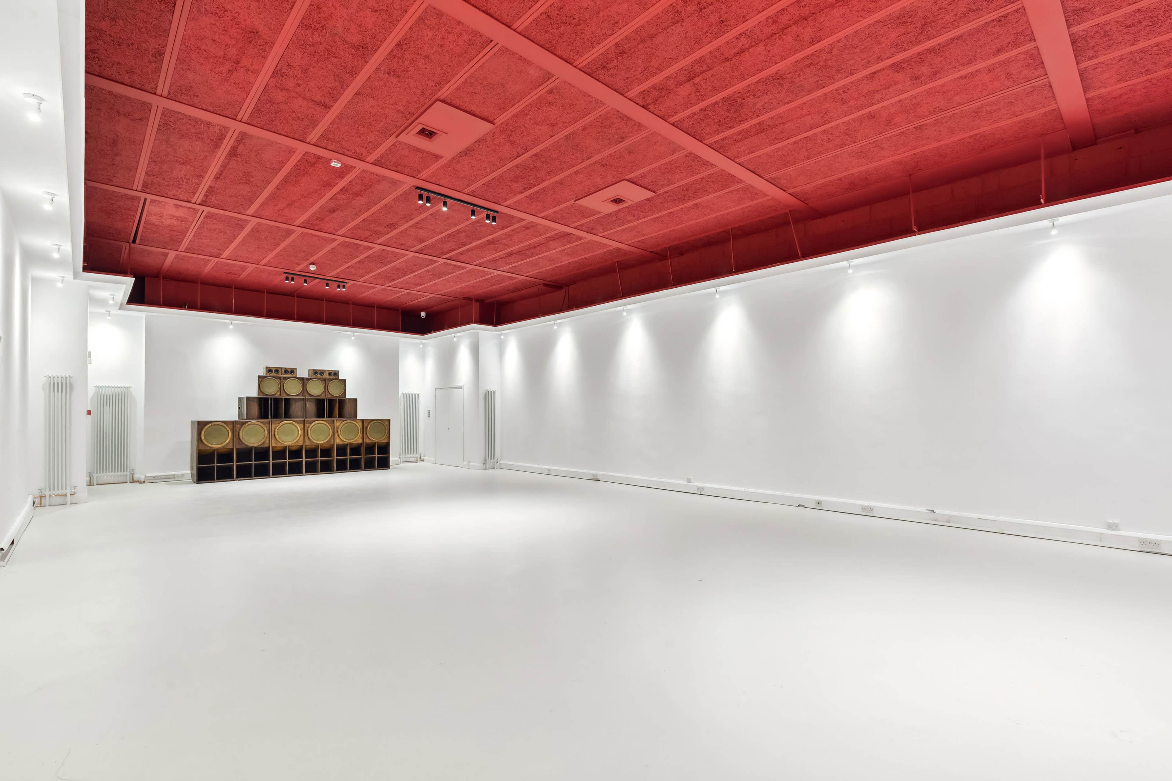 A spacious, empty room with white walls and a red ceiling, featuring a stack of circular wooden objects against one wall.