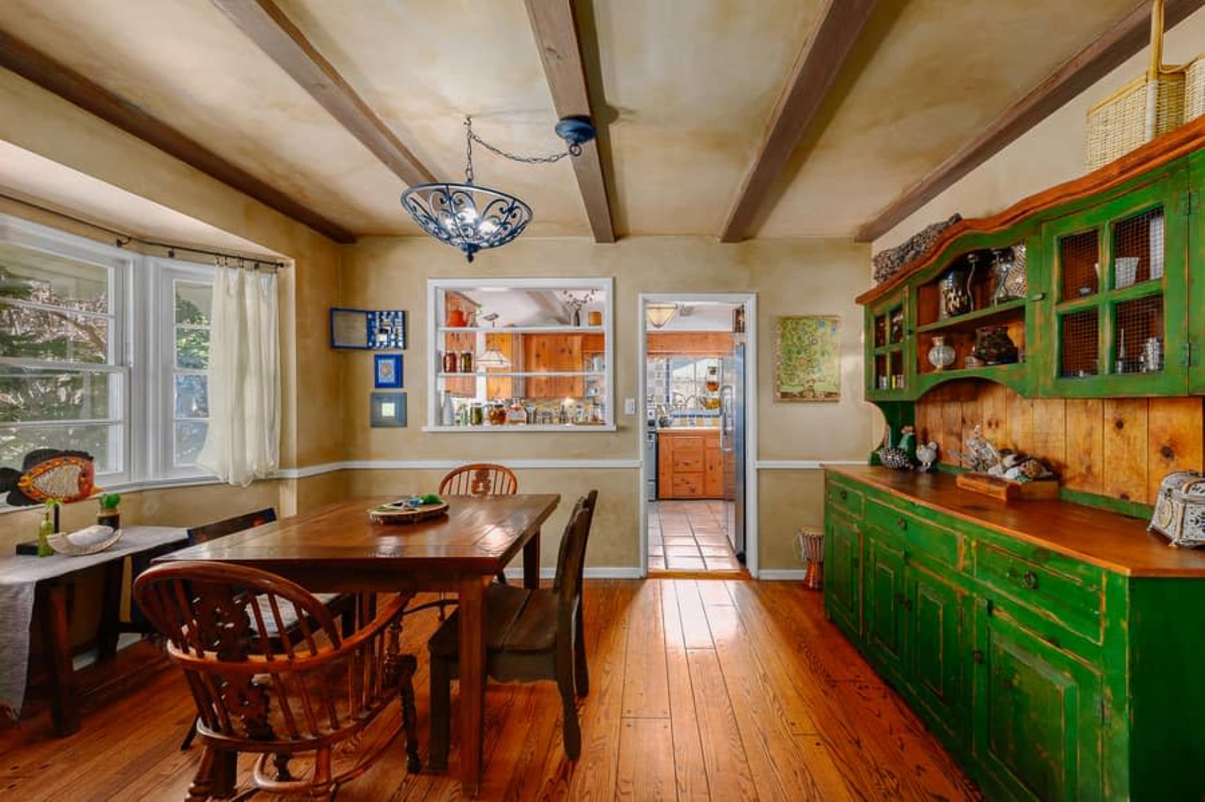 A rustic dining area with a wooden table and chairs, a green wooden sideboard, and exposed ceiling beams.