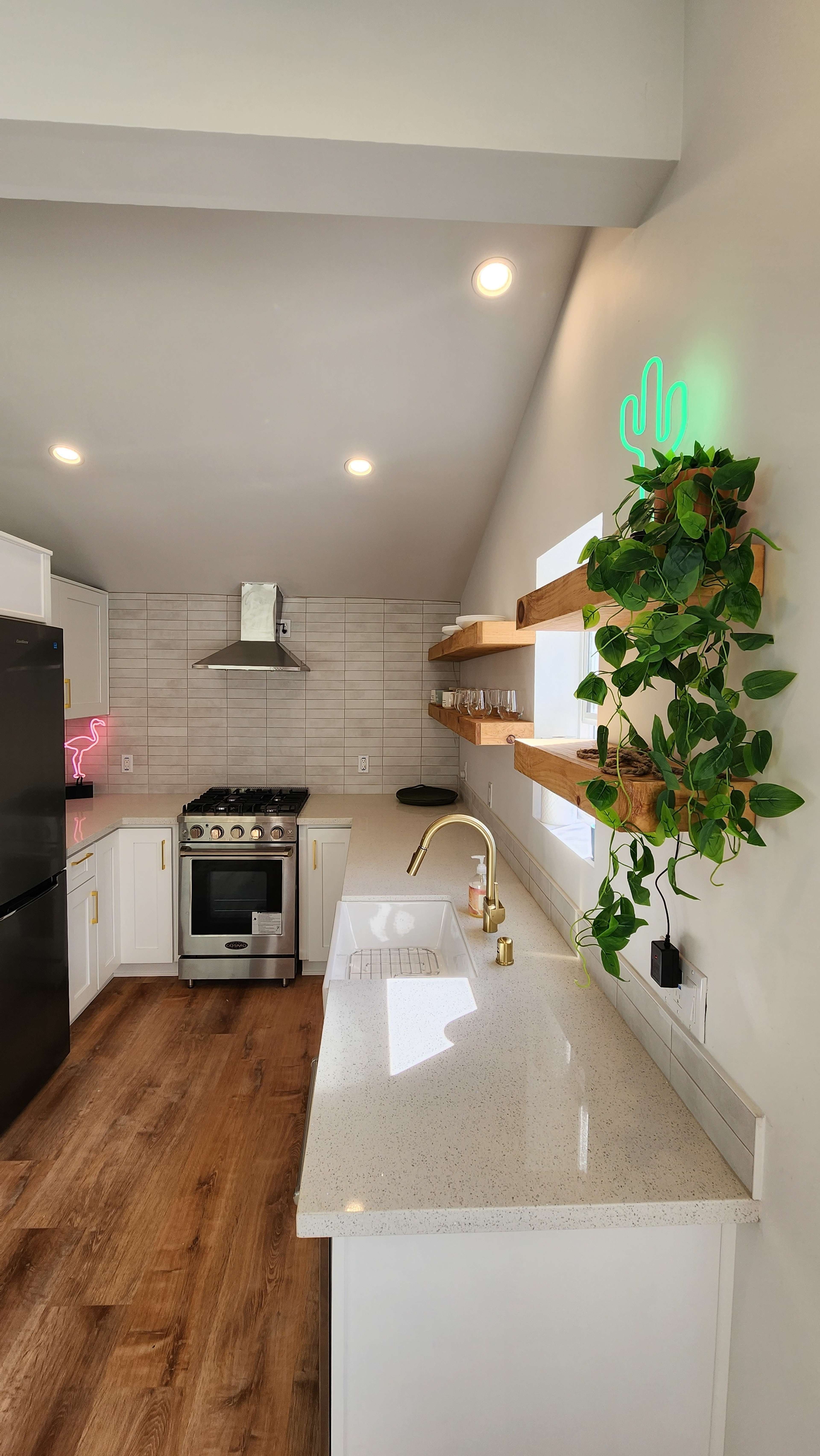 The image shows a modern kitchen featuring white cabinets, a gas stove, and wooden shelves adorned with plants.