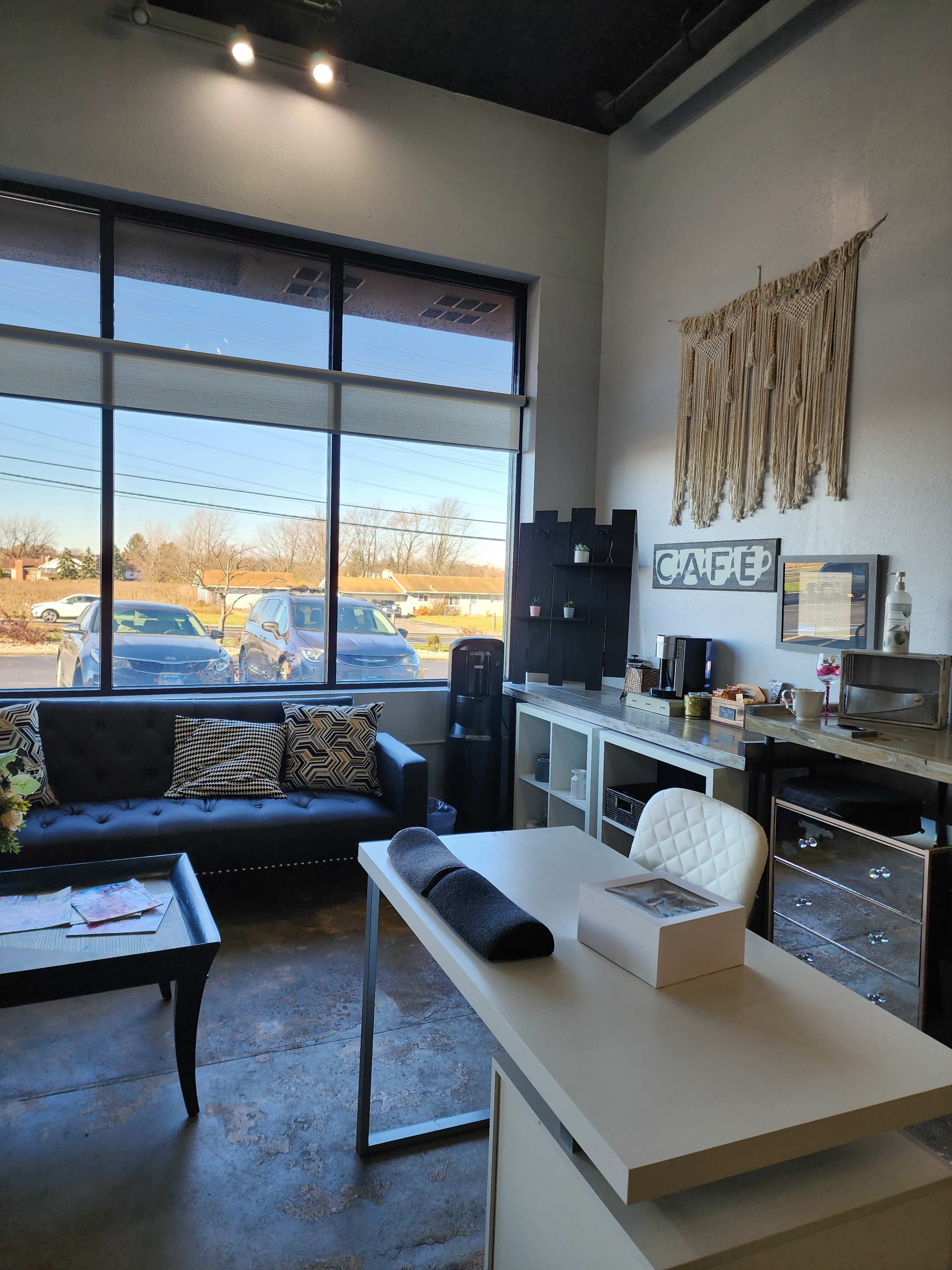 A modern cafe interior with a seating area, a desk, and large windows displaying parked cars outside.