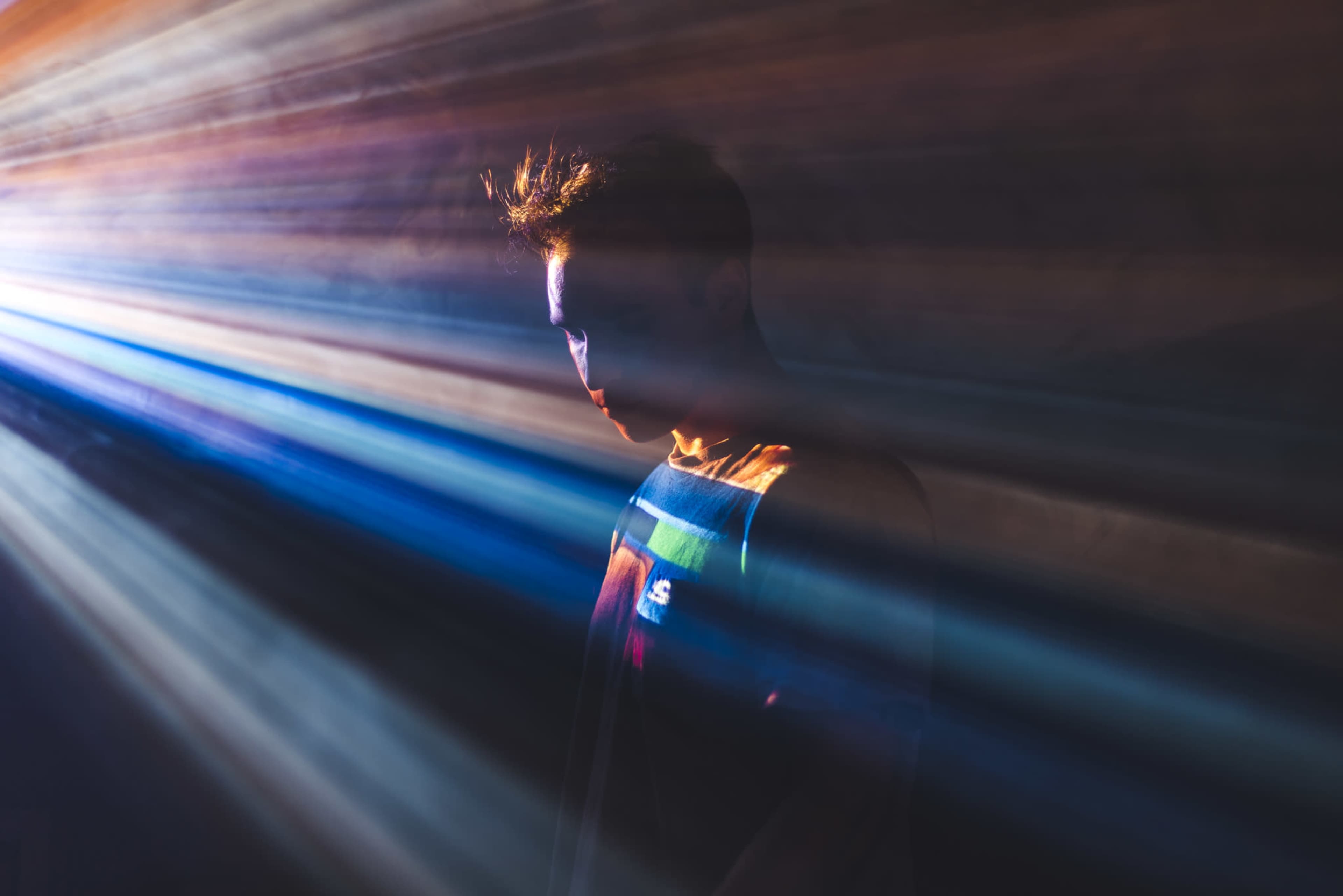 A person stands in a dimly lit environment with colored light rays streaming around them.
