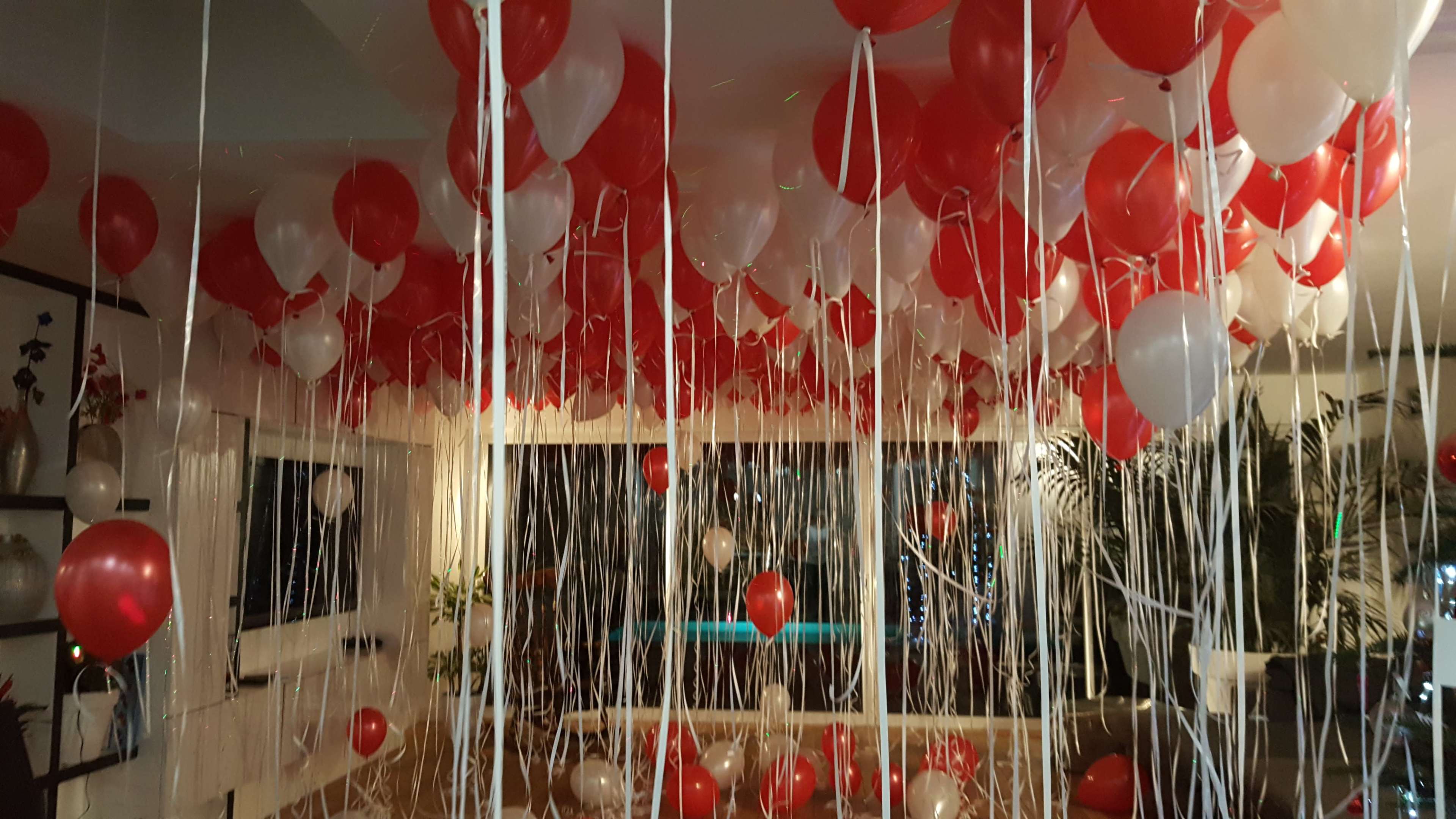 The room is filled with red and white balloons hanging from the ceiling, creating a festive atmosphere.