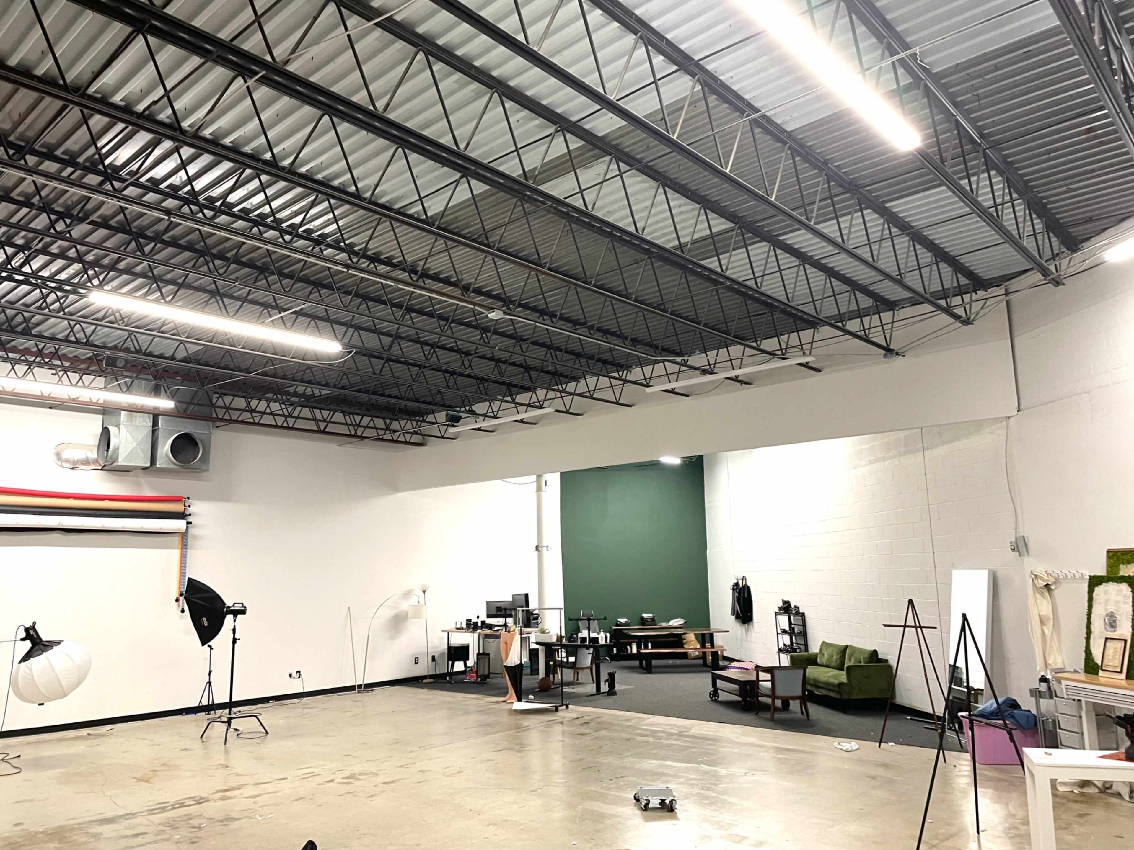 The image shows a spacious room with high ceilings featuring divided areas for a photography studio and a lounge, equipped with various furniture and equipment.