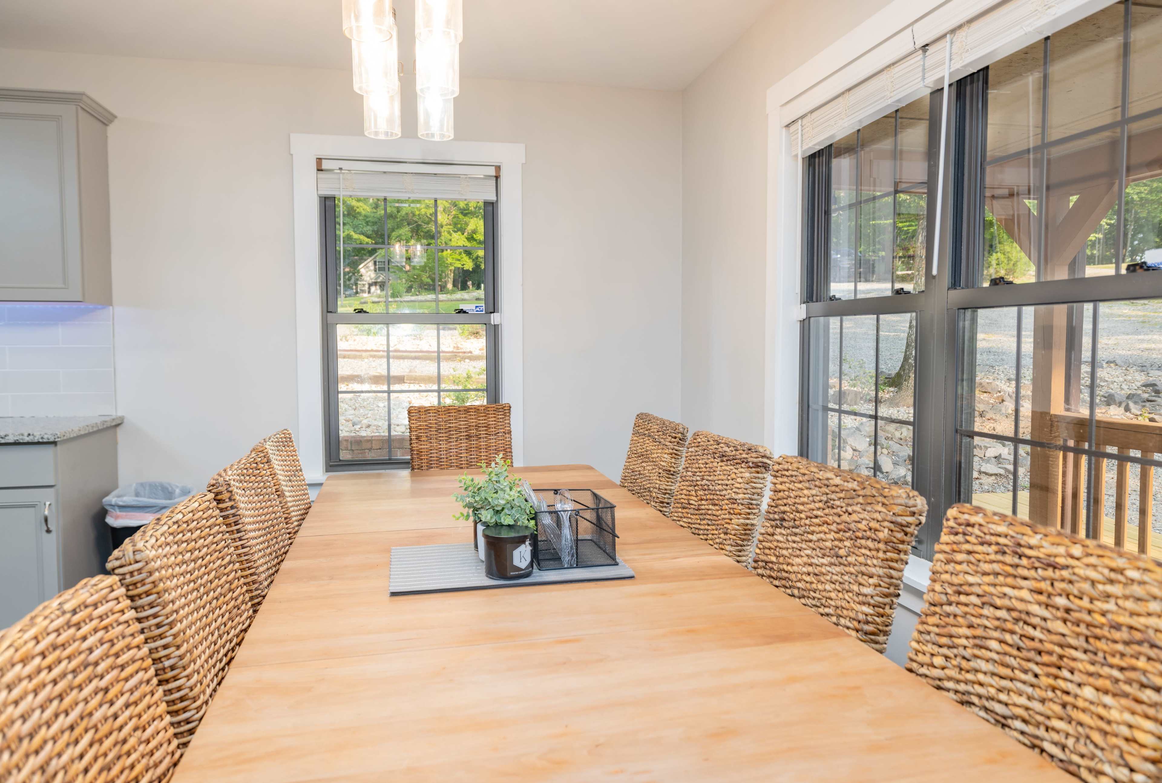 A spacious dining area features a wooden table surrounded by woven chairs, with large windows providing natural light.