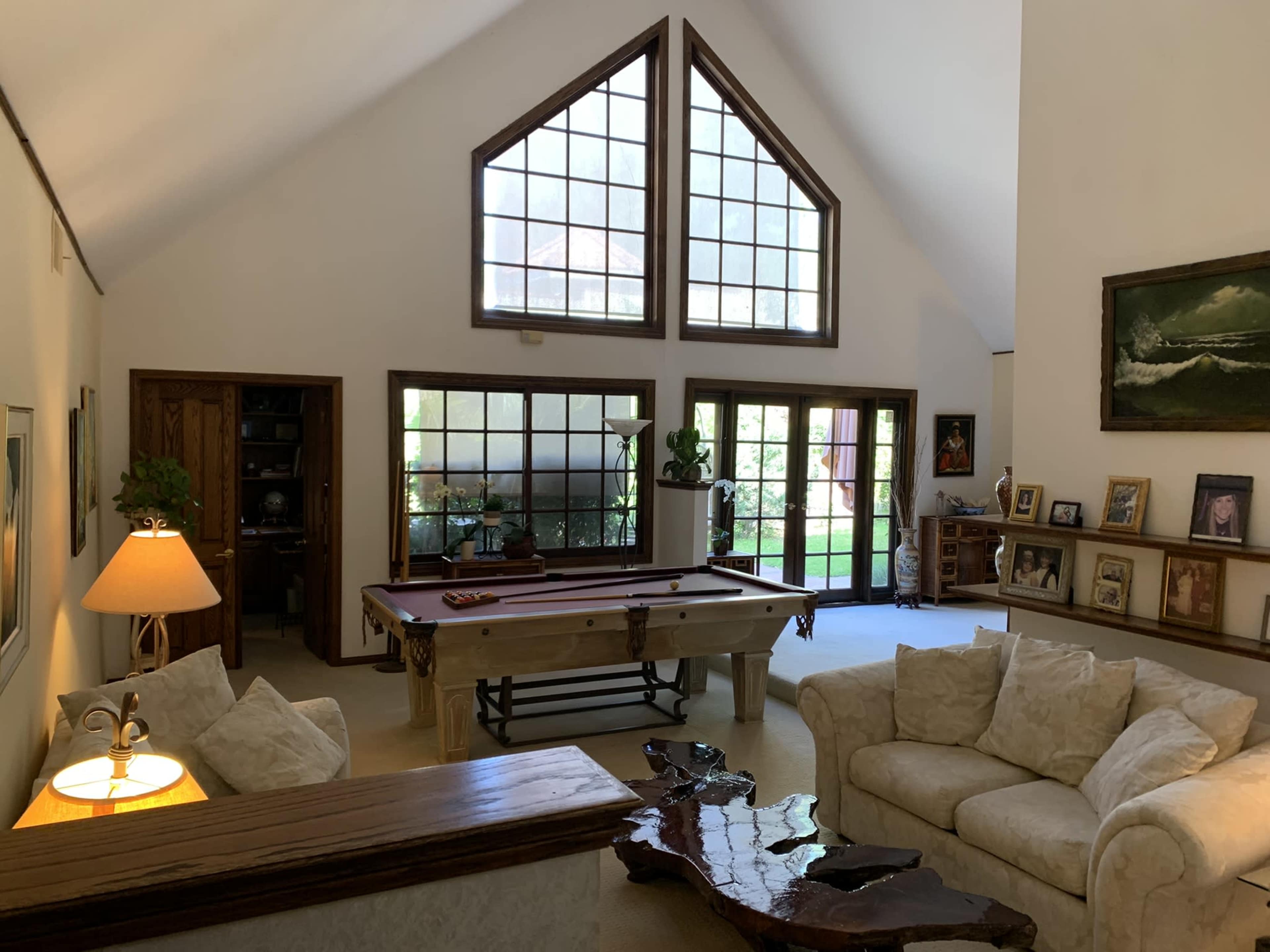 A spacious living room with a high ceiling, large windows, a pool table, and a cozy seating area.