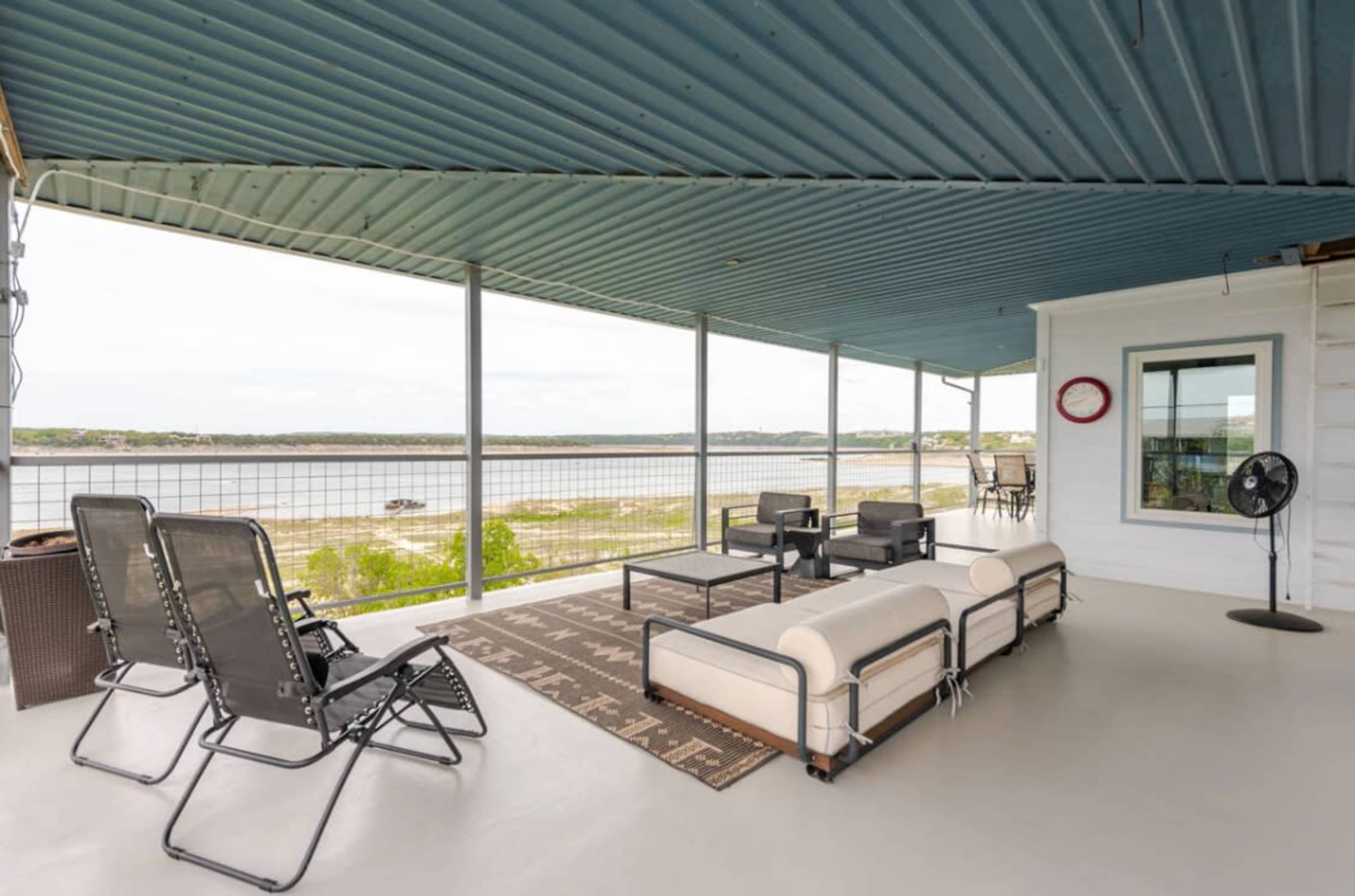 The image shows a spacious porch overlooking a lake, equipped with outdoor furniture and a ceiling painted in blue.