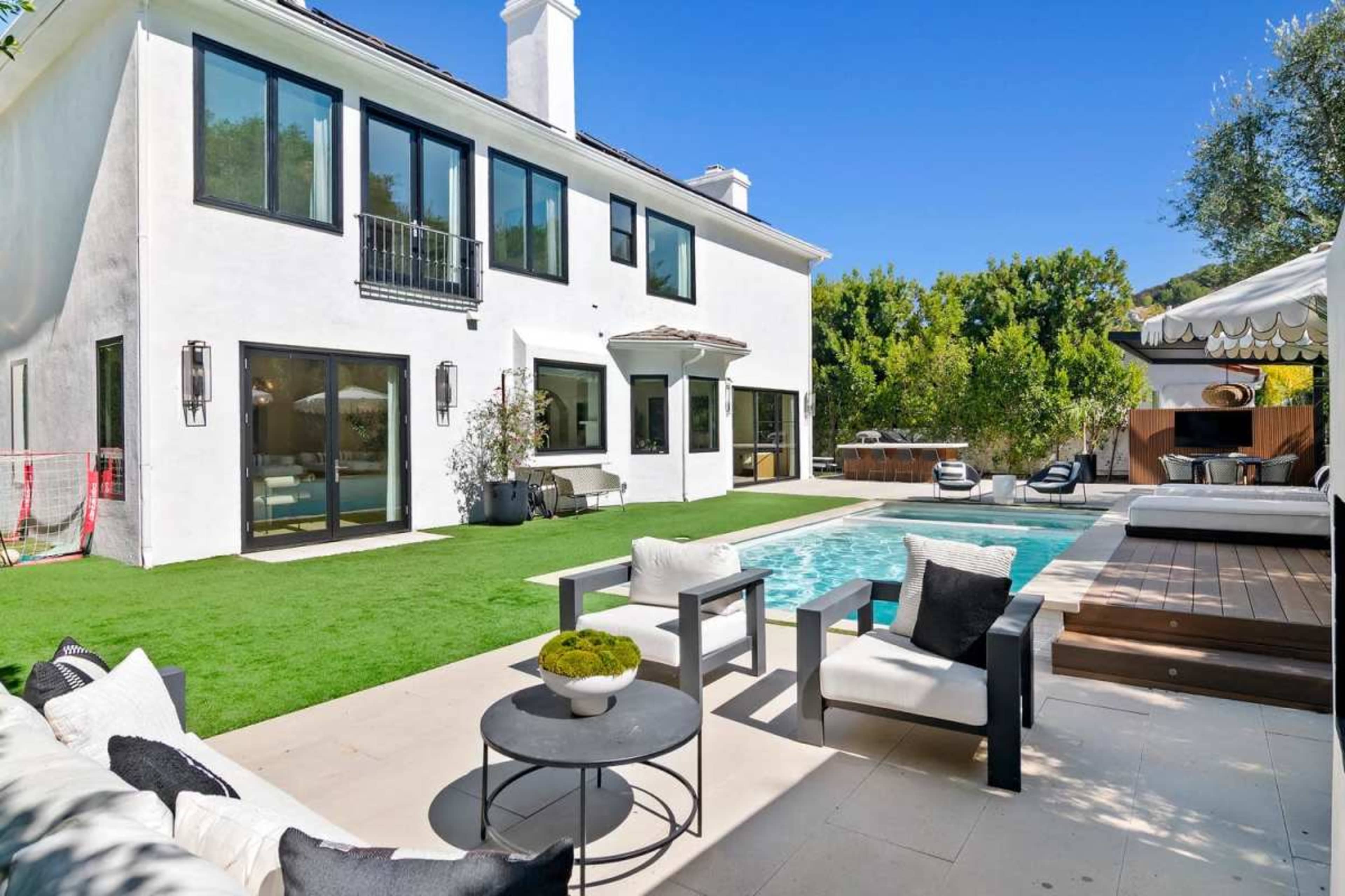 The image shows a modern home with a swimming pool and a well-maintained lawn, featuring outdoor seating and a patio area.