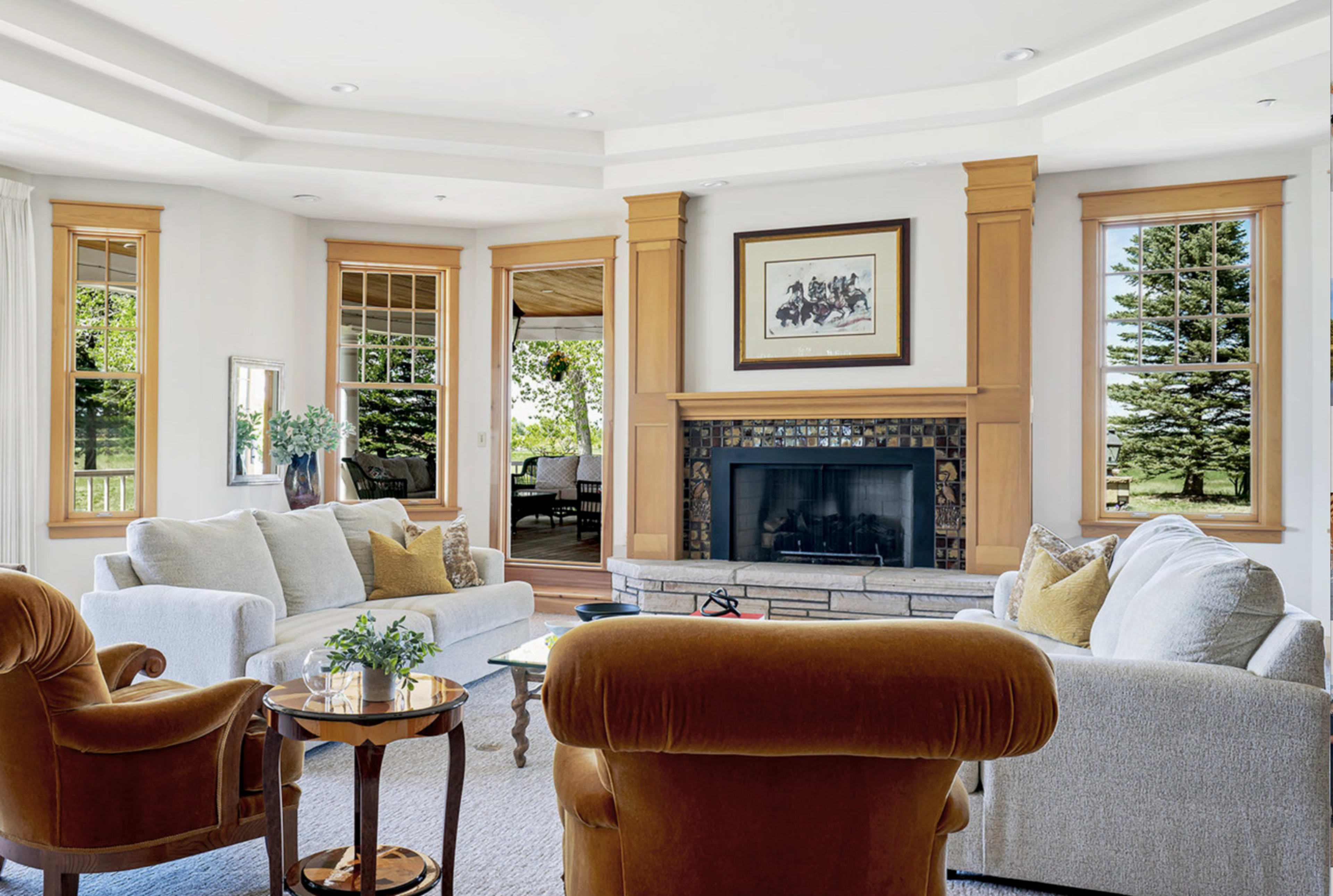 The image shows a spacious living room featuring a fireplace, large windows, and two distinct seating areas with a round table in the center.