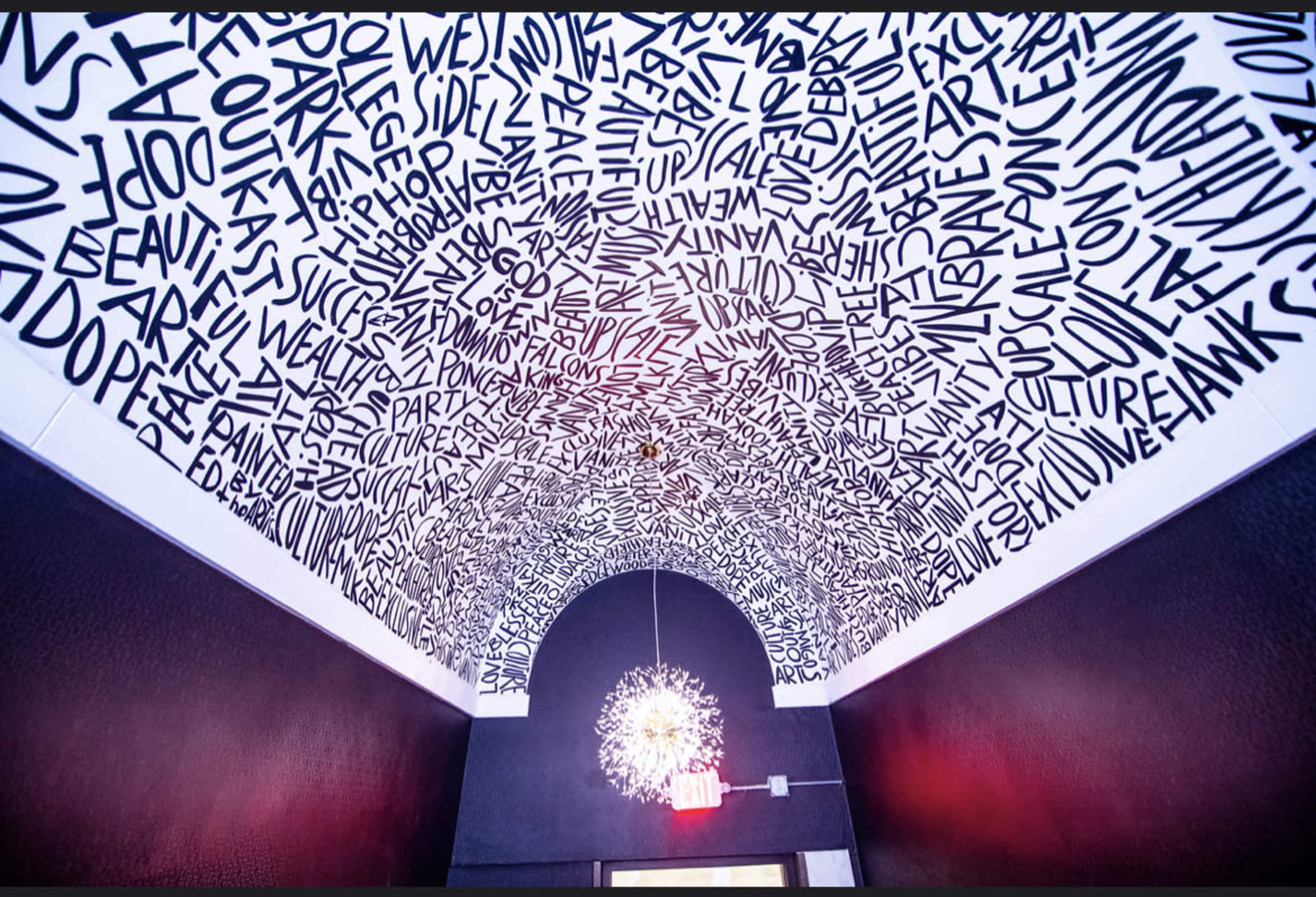 The ceiling of a room is covered with intricate black-and-white text in various fonts and sizes, while a modern light fixture hangs in the center.
