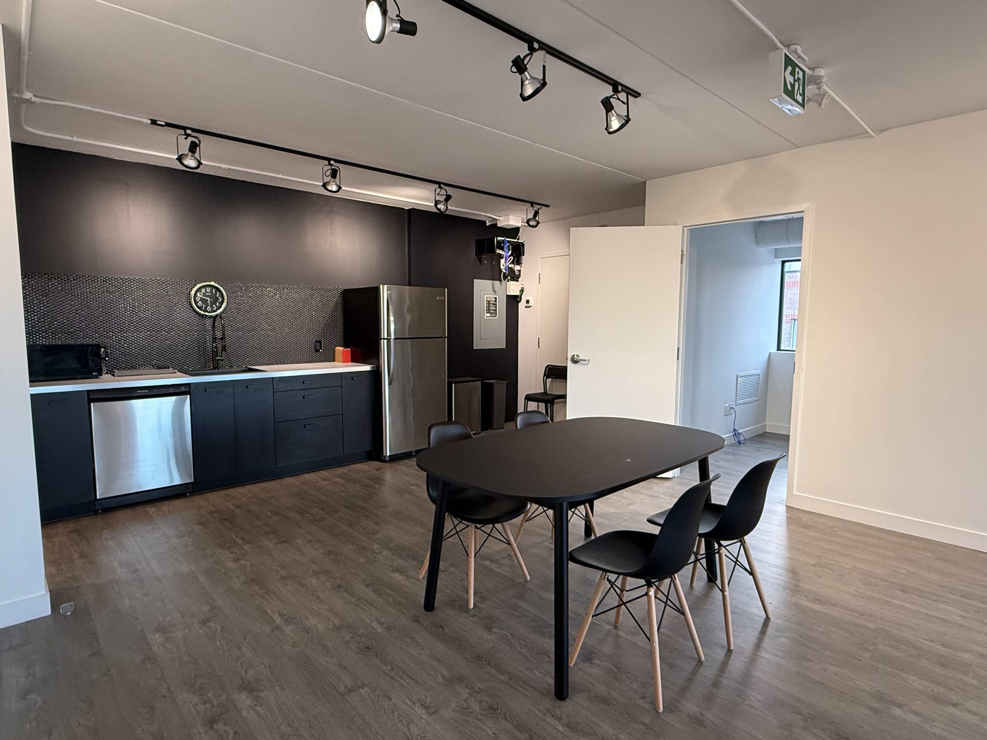 The image shows a modern kitchen and dining area featuring a black table with four chairs, stainless steel appliances, and a contrasting black and white color scheme.