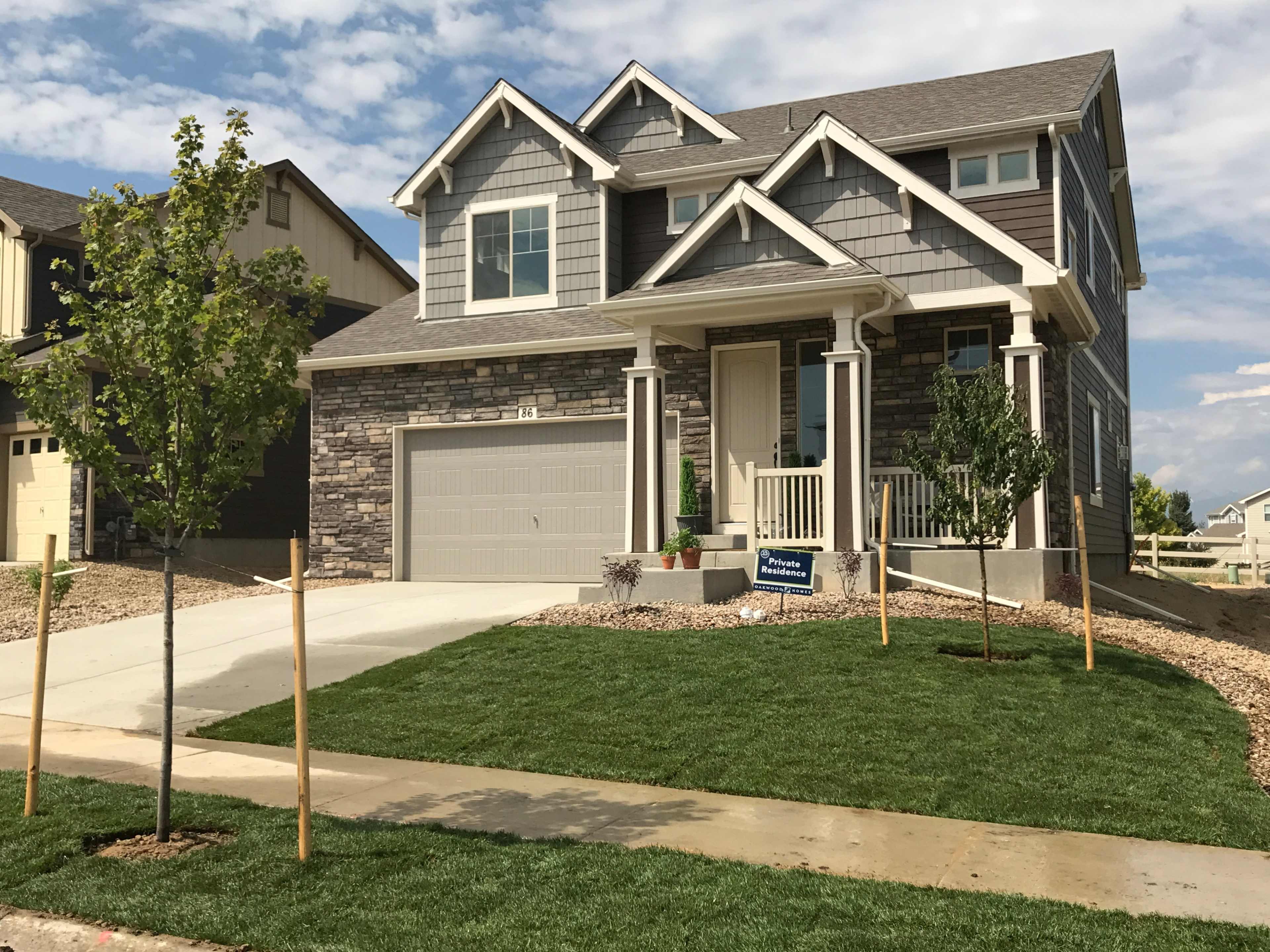 A two-story house with stone and siding exterior features a front porch, garage, and freshly landscaped lawn with young trees.
