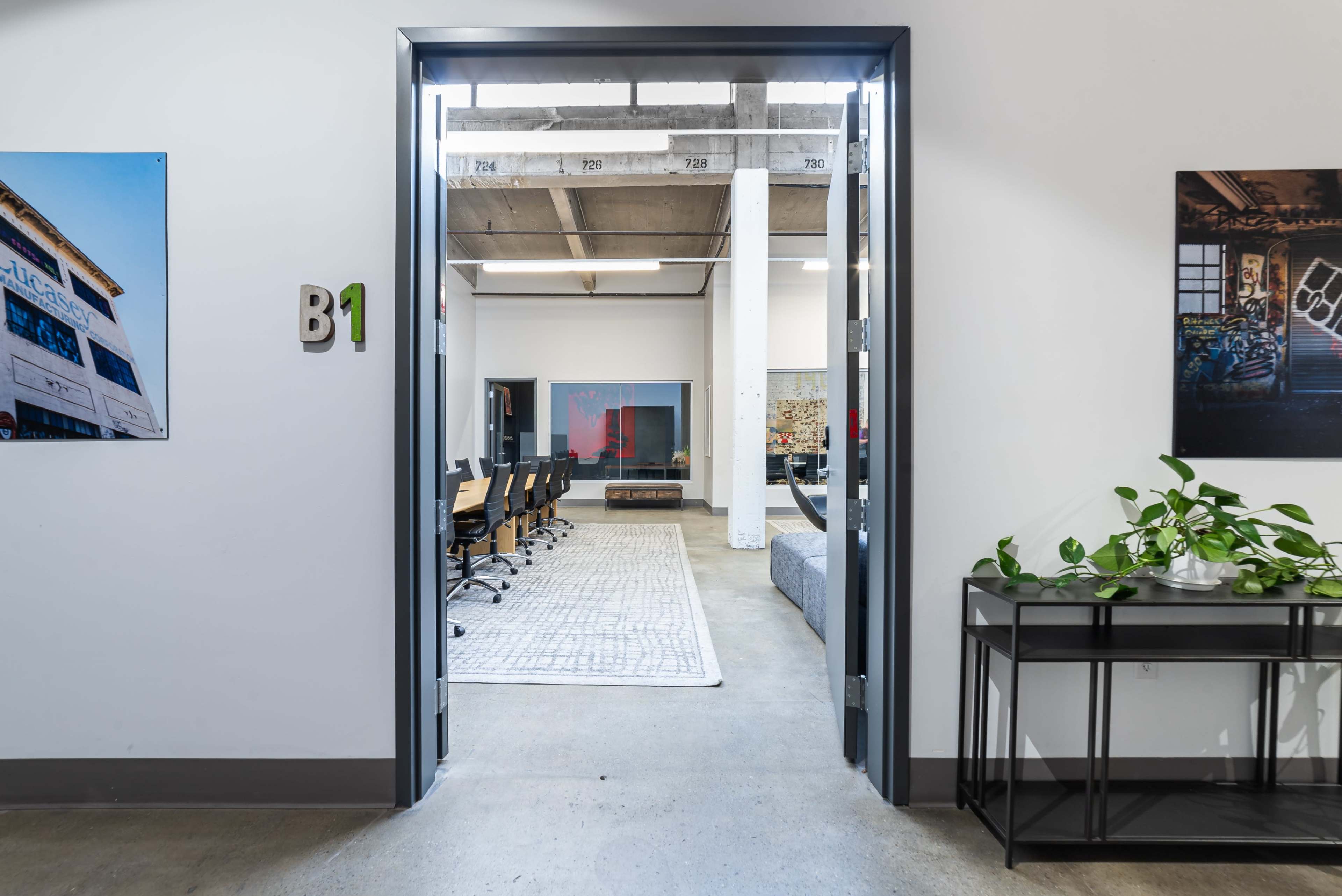 A hallway leads to a meeting room featuring multiple chairs and a large table, with artwork displayed on the walls.