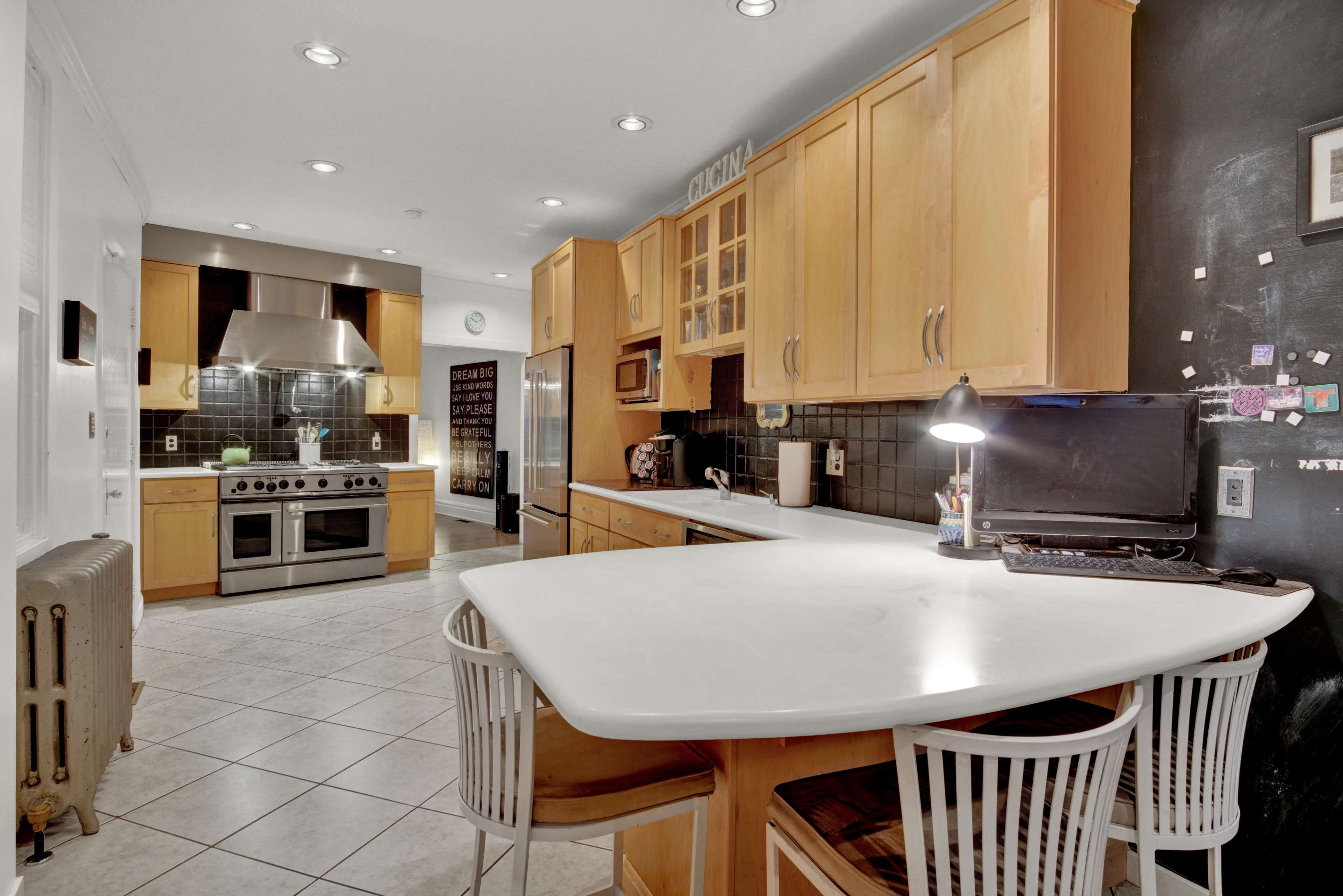 A modern kitchen with wooden cabinetry, stainless steel appliances, and a white countertop with bar stools.