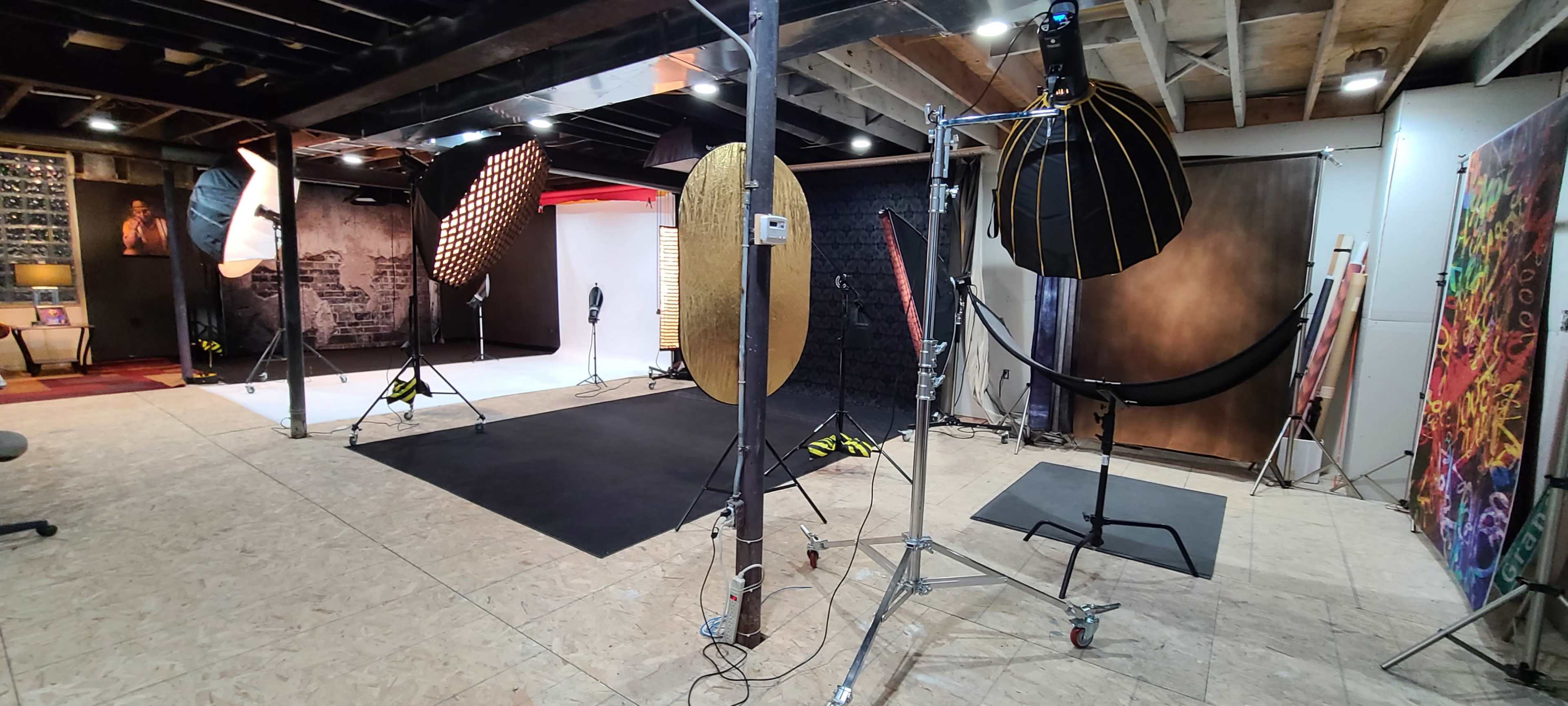 A photography studio with various backdrops, lighting equipment, and set pieces arranged on a wooden floor.
