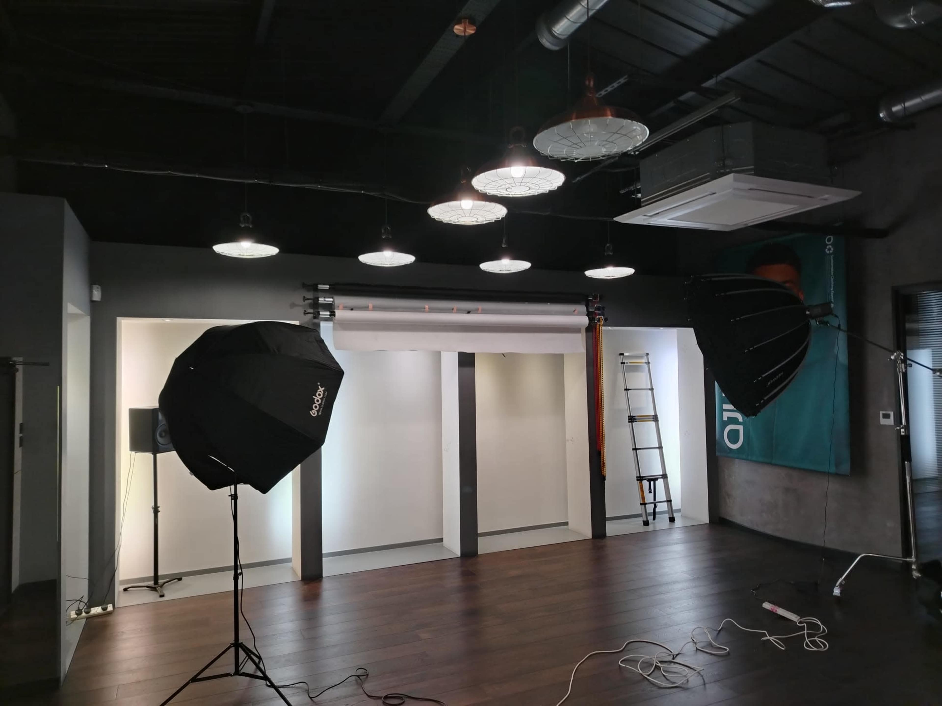 The image shows a photography studio setup with two large softbox lights, a backdrop, and a ladder against the wall.