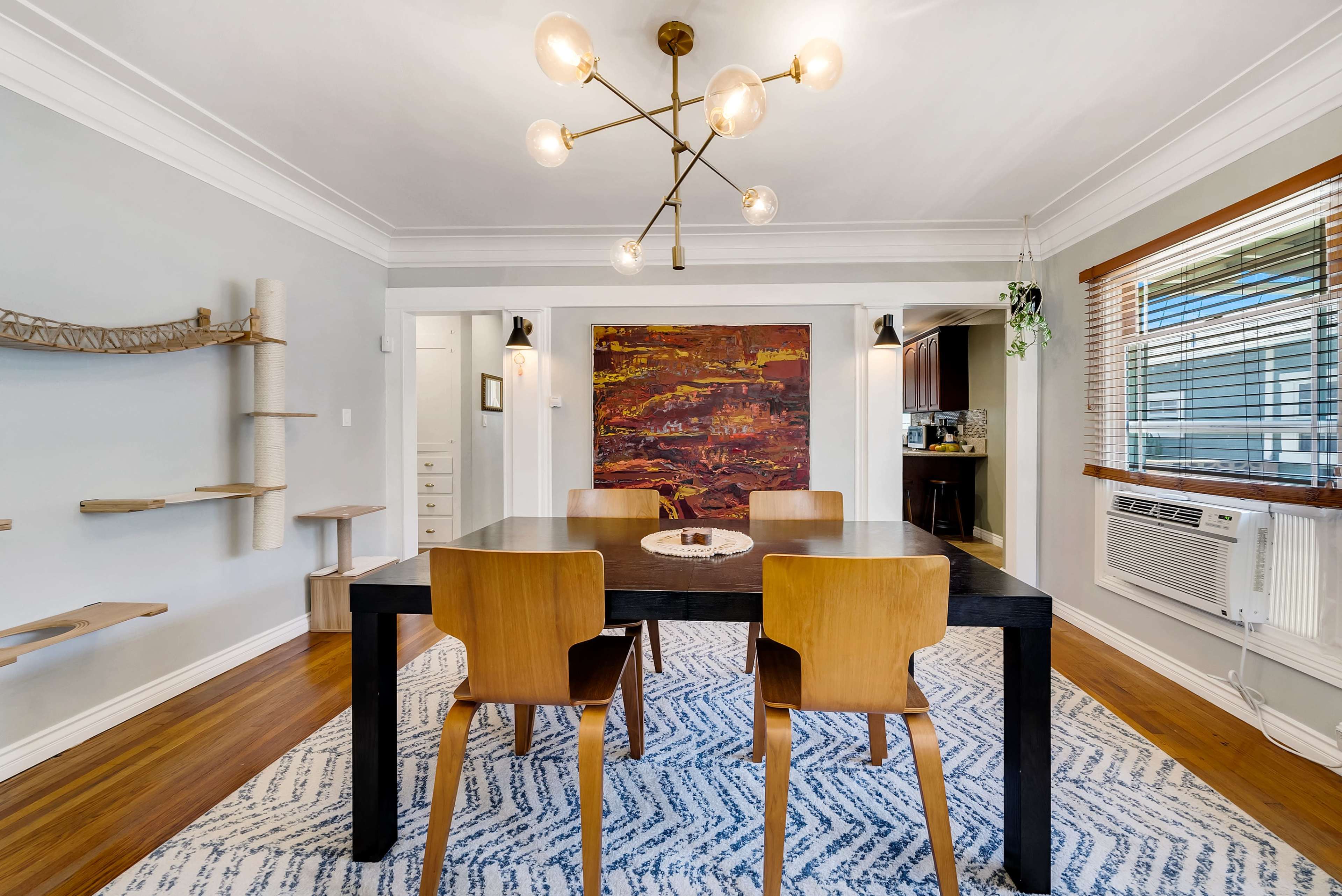 A modern dining room features a black table with wooden chairs, a large abstract painting on the wall, and a geometric light fixture above.