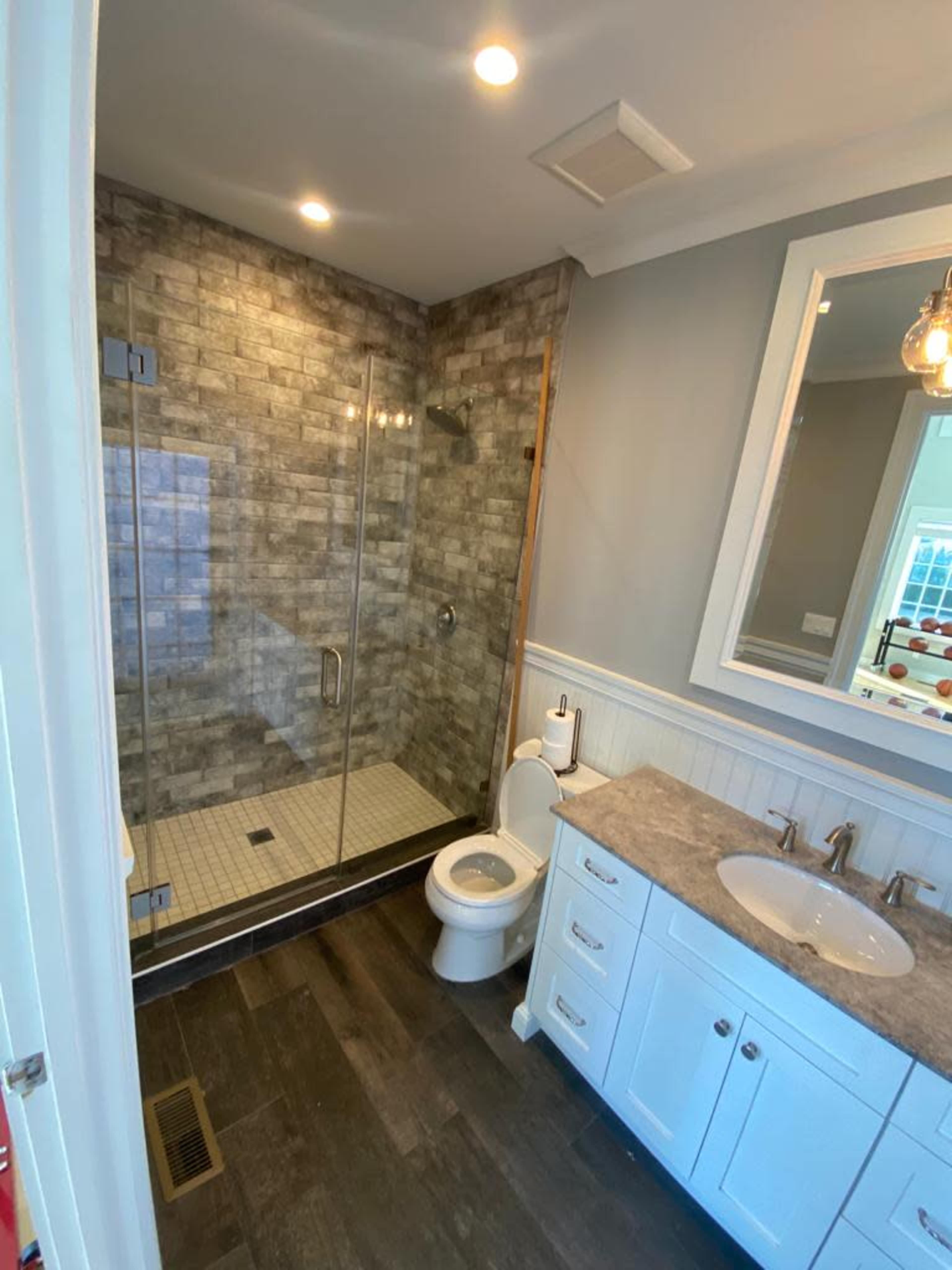 The image shows a modern bathroom featuring a glass-enclosed shower, a toilet, and a double-sink vanity with a gray countertop.