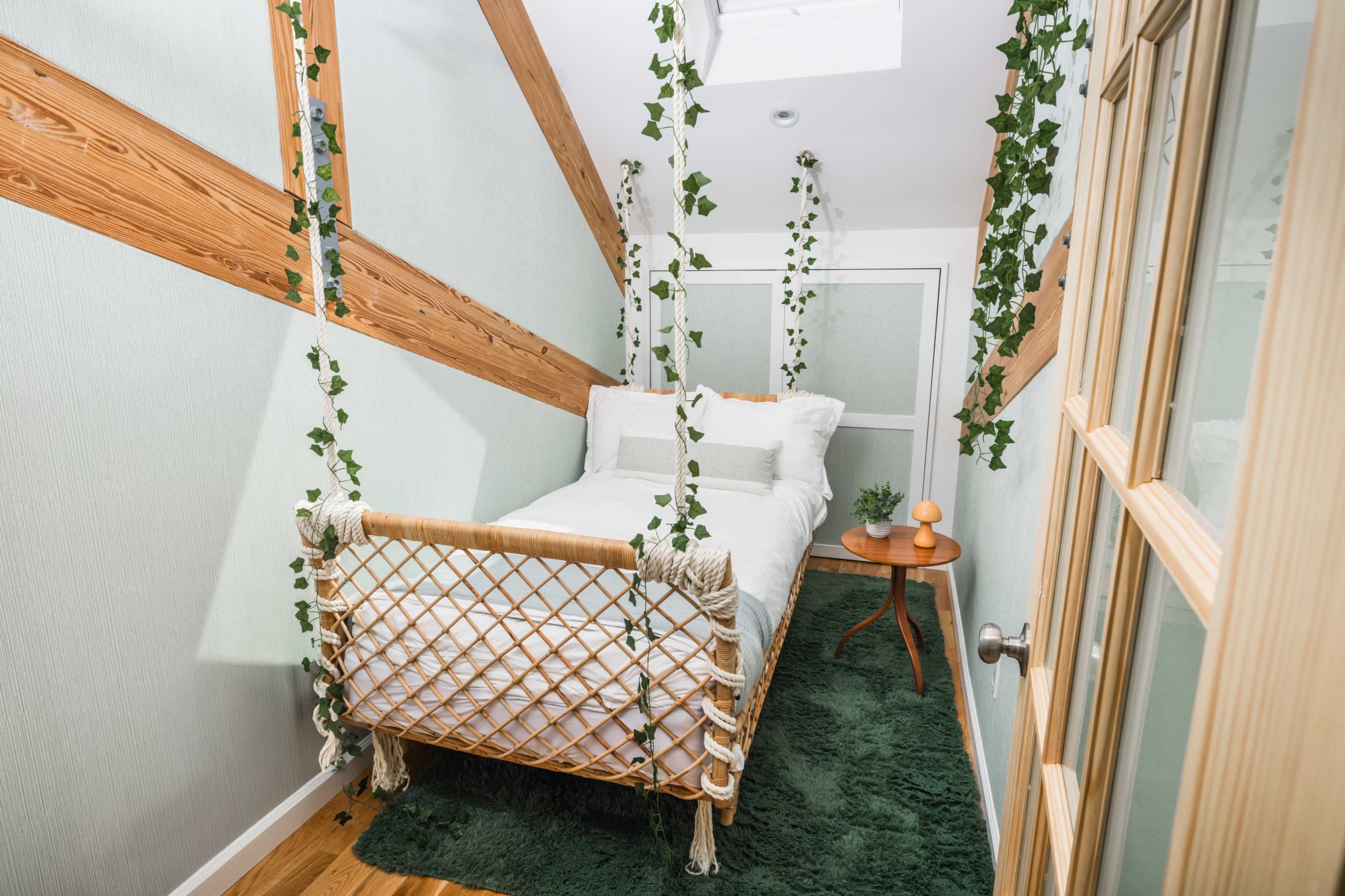 A small bedroom with a suspended bed framed by green walls and wooden beams, adorned with trailing plants.