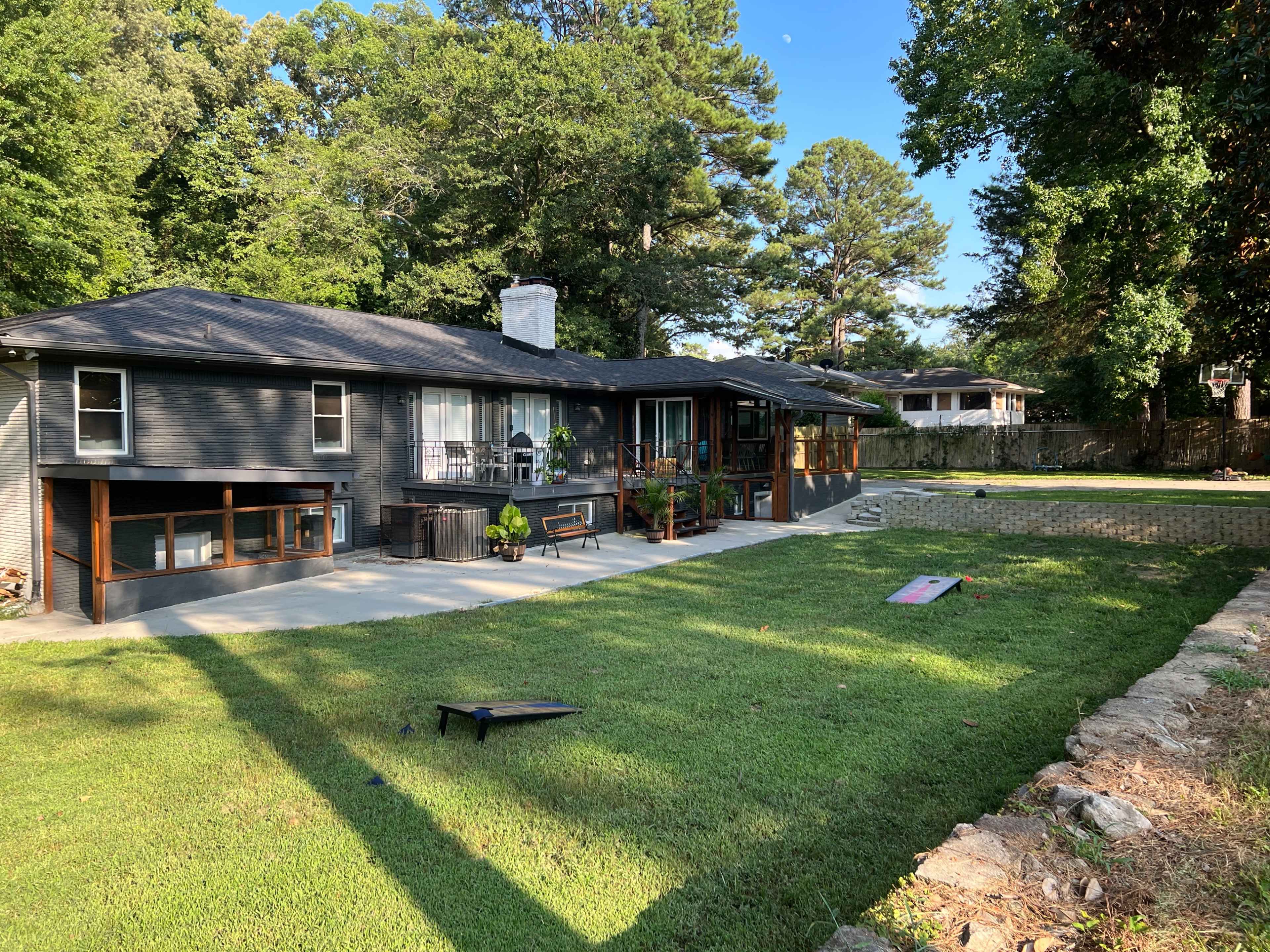 A modern, single-story house with a large patio area and a well-manicured lawn surrounded by trees.