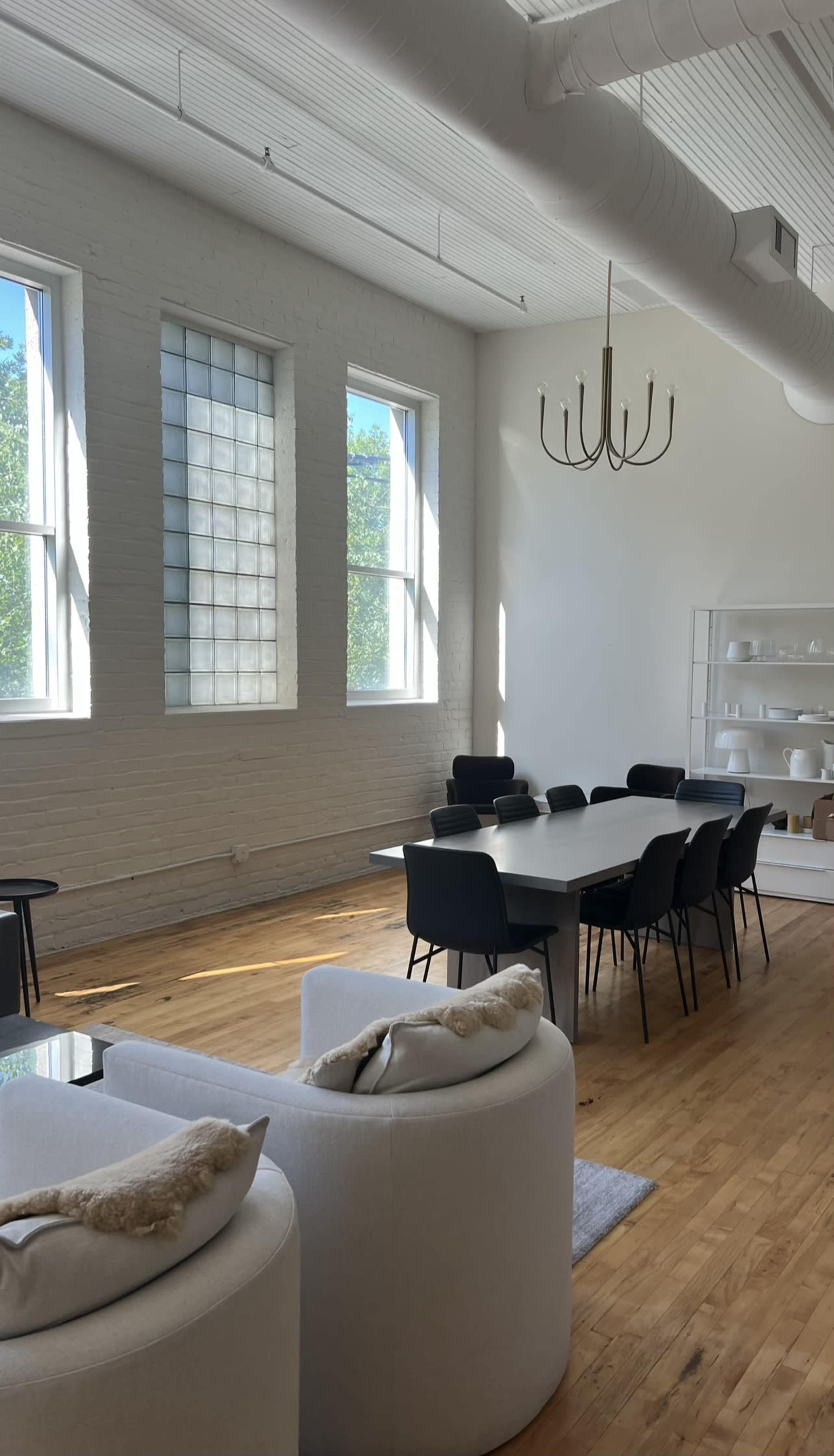 A spacious dining area features a large white table surrounded by black chairs, with large windows allowing natural light to illuminate the room.