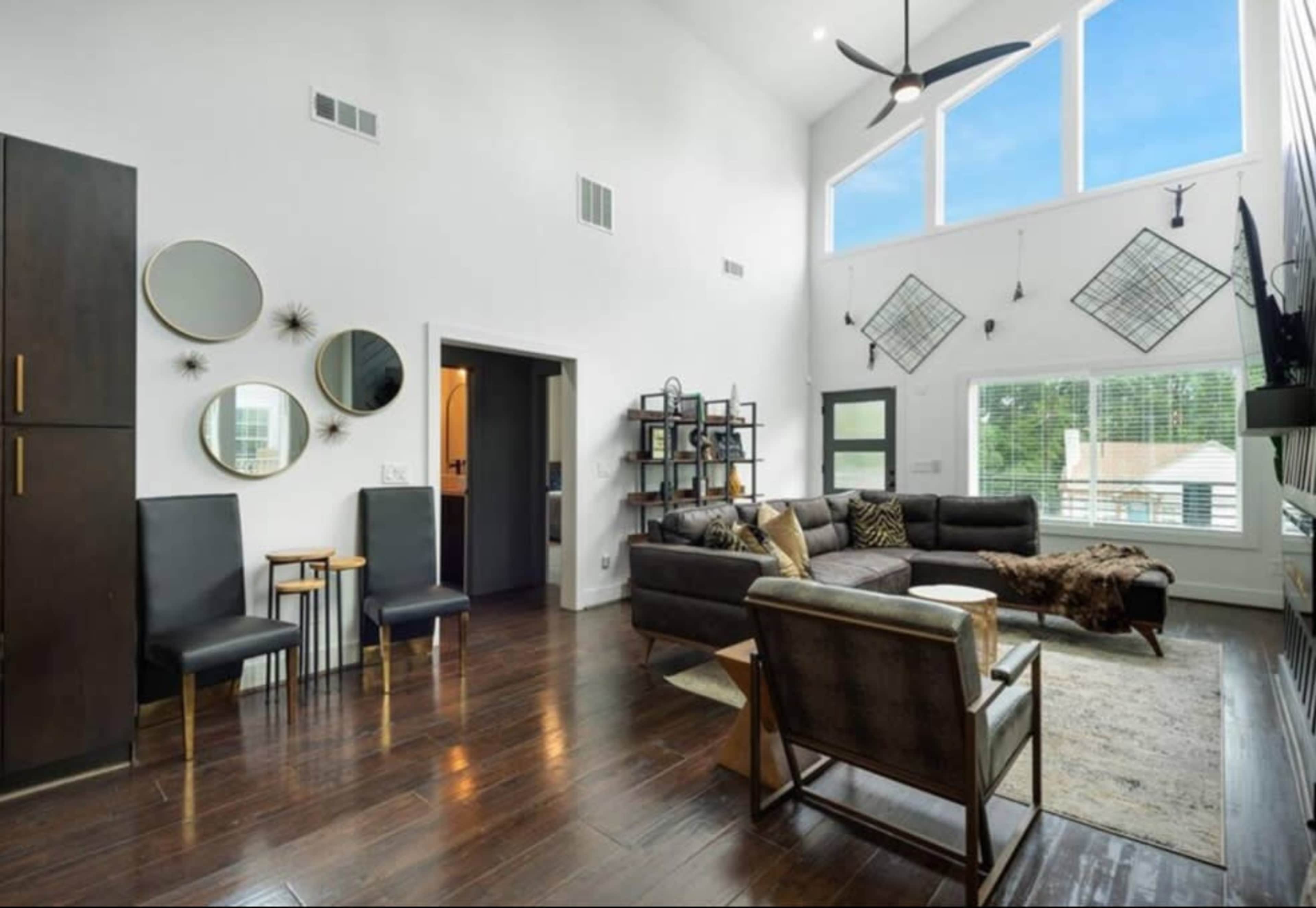 The living room features high ceilings with large windows, modern furniture, and decorative wall elements.