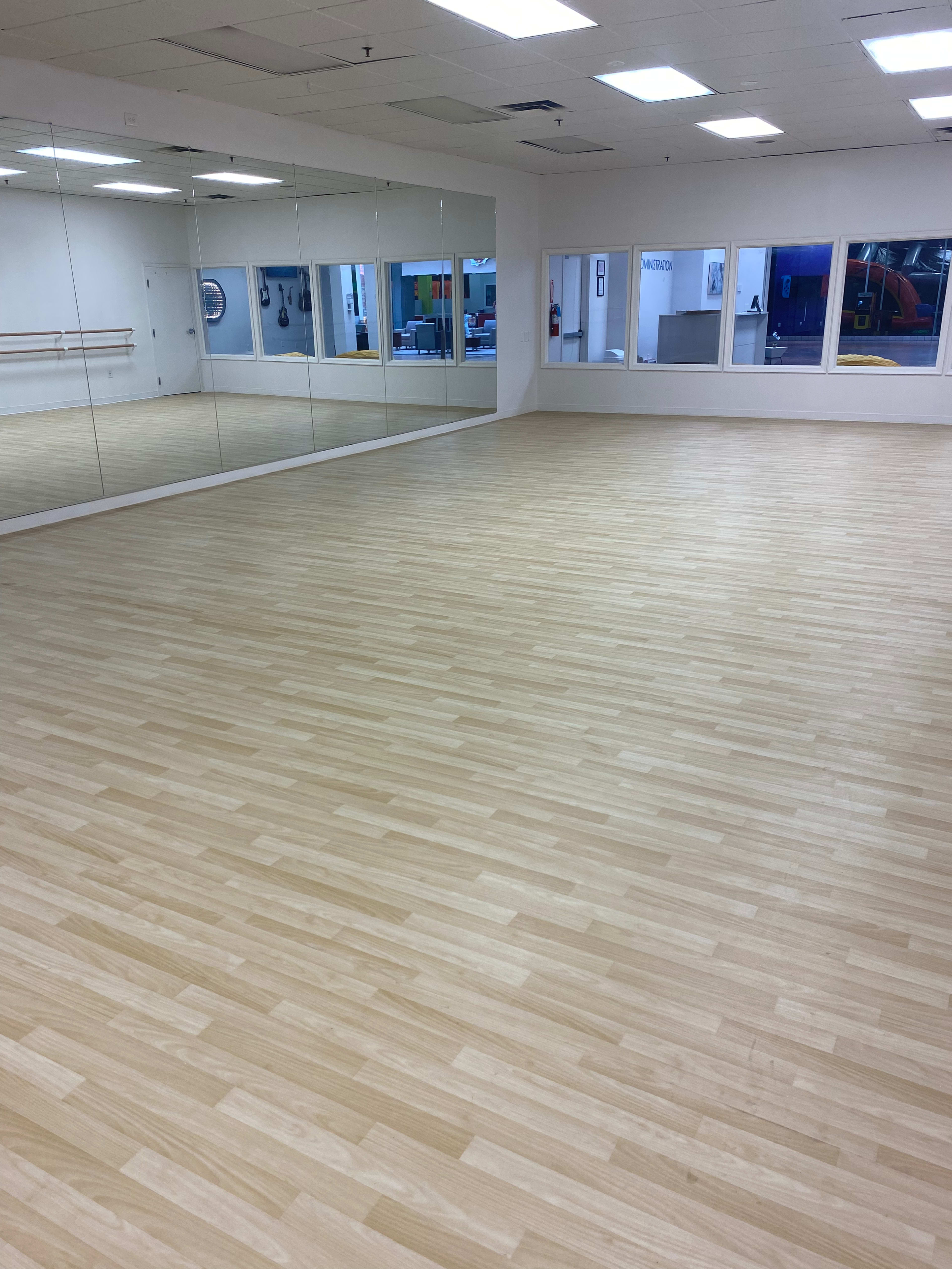 A spacious dance studio with wooden flooring and large mirrors on one wall.