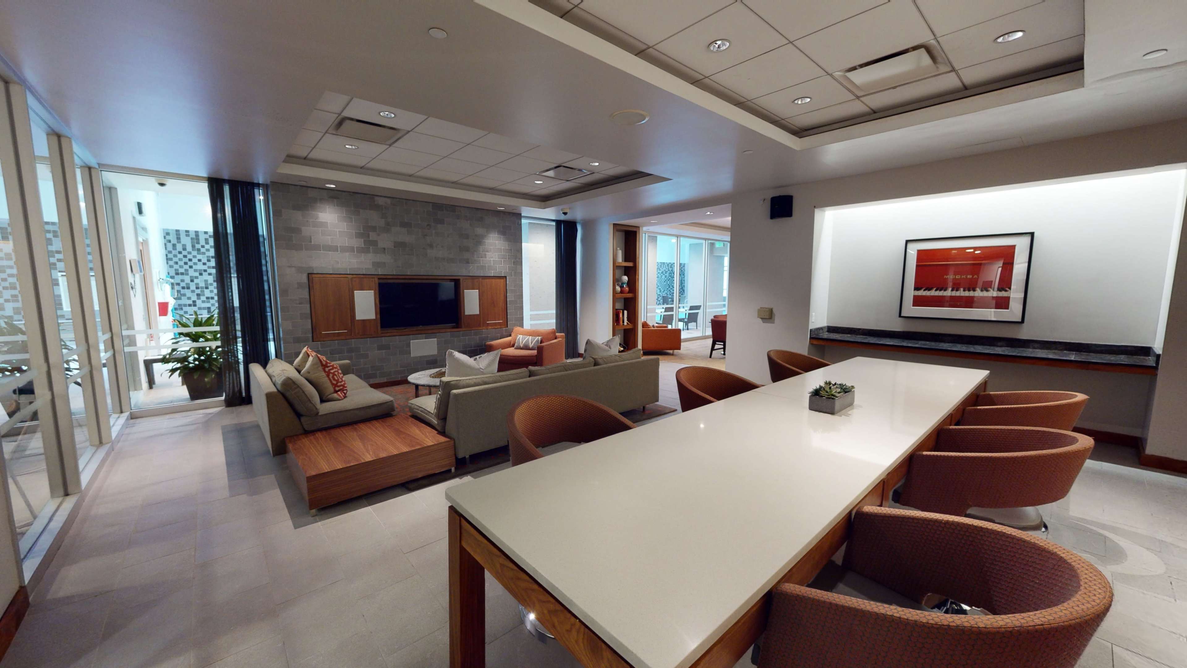 A modern lounge area with comfortable seating, a large table, and a television on the wall.