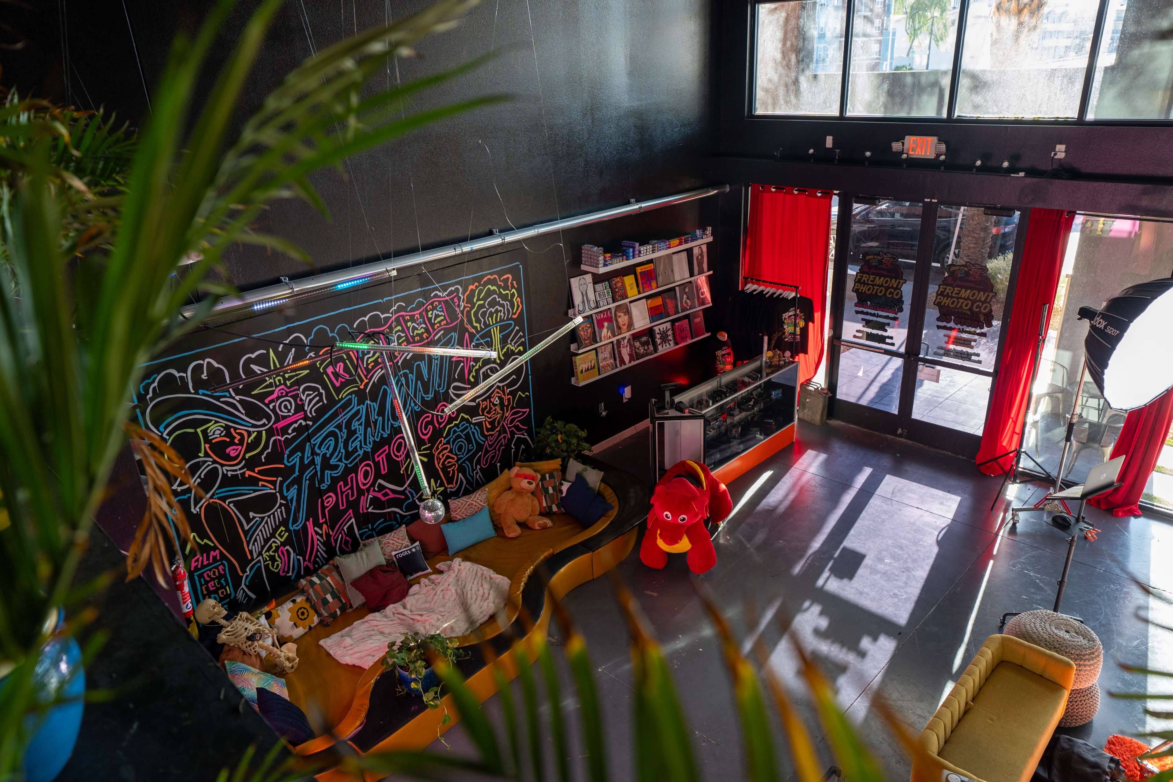 A brightly colored photography studio with a cozy seating area, bookshelves, and a large window adorned with red curtains.