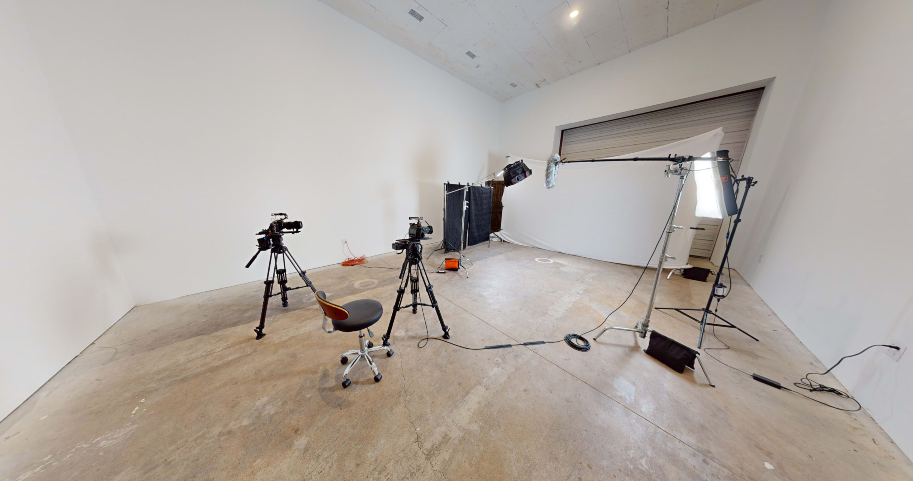 A photography studio equipped with several cameras on tripods, lighting equipment, and a backdrop set up against a plain wall.